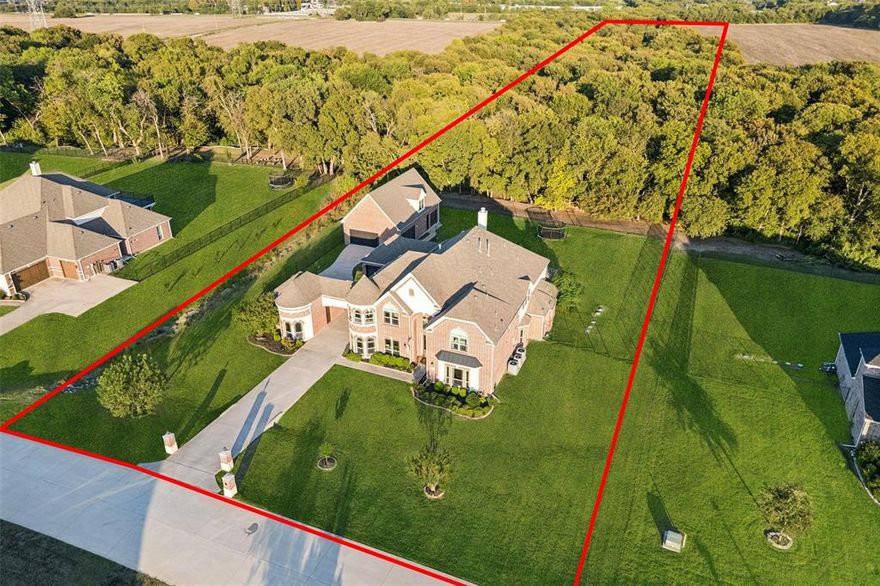 Price per square foot DOES NOT include the 2,000-square-foot detached addition! Discover a Private Retreat—an exceptional family estate offering nearly 8,000 square feet of combined living space across the main home, guest house, and ultimate man cave, all set on 2.65 acres backing to a wooded creek. Brick and stone architecture, turret accents, and mature landscaping create striking curb appeal. Inside, vaulted beamed ceilings, rich wood flooring, and brick details define the open-concept living spaces. The chef’s kitchen is equipped with Electrolux appliances, double ovens, granite countertops, a prep sink, reverse osmosis system, and generous cabinetry. A spacious game room and media room with Sony projector, surround sound, wet bar, and wine fridge are designed for seamless entertaining. The downstairs primary suite features a sitting area and spa-like bath with stone finishes and a multi-head rain shower, while a private in-law suite offers ideal guest accommodations. Outdoor amenities include a covered patio, pergola, built-in kitchen, fireplace, pool with spa and waterfalls, and a nearby firepit for year-round enjoyment. The detached guest house includes a home office, private guest quarters, and a man cave with industrial finishes, bar, gym space, and high-speed wired connectivity—perfect for guests, multi-generational living, or game-day gatherings. A rare opportunity to own a guest house of this scale in Lucas, complete with two 2-car garages and a portecochere for ample parking. This property delivers a seamless balance of luxury, versatility, and everyday comfort.