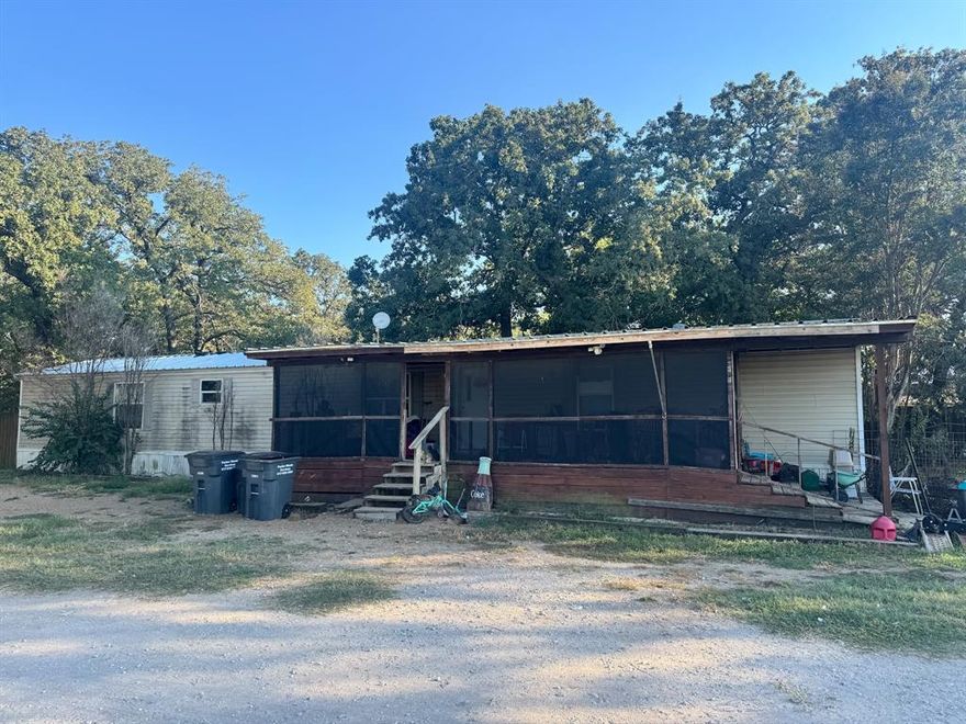 Come check out this mobile home on a 1-acre treed lot that sits towards the end of a cul-de-sac in Springtown ISD. Home sits toward the back of property with detached 2 car garage, not finished out on inside. Has another metal shop with 2 covered parking areas up front and 2 enclosures in back. Home is running off water well that is inside one of these enclosures. Home has oversized screened in front porch, custom cabinets, oversized bedrooms and bathrooms with custom tile in showers. Additional bedroom was added on back of home with covered outdoor patio area. Plenty of yard space with separate fenced in area with oversized chicken coop. New metal roof put on in 2024. Home sold AS IS