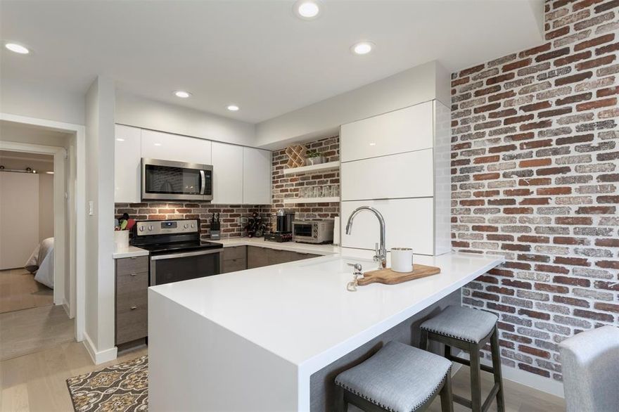 Experience refined living in this exquisite 1-bedroom, 1.5-bath residence thoughtfully renovated and located in the coveted Boardwalk on the Parkway community. Positioned on the first floor, this sophisticated condominium offers 985 square feet of curated interiors where timeless comfort meets modern design. The chef-inspired kitchen is a true showpiece, featuring custom cabinetry including horizontal bifold cabinets, dramatic waterfall-edge countertops at the peninsula, and a striking brick-style backsplash that seamlessly extends into the dining space—creating a cohesive, high-end aesthetic. Thoughtful details continue with modern barn-style doors concealing the pantry and stackable washer and dryer, blending function with architectural interest. The living area exudes warmth and elegance, anchored by a wood-burning fireplace and enhanced by built-in shelving, a wet bar, dual pane low-e windows and abundant storage—ideal for both intimate evenings and elevated entertaining. Step outside to your private, fenced patio, a serene retreat perfect for morning espresso or evening wine. Residents enjoy access to a sparkling community pool, manicured grounds, and the convenience of an enclosed carport with additional storage. Ideally situated in North Dallas near premier shopping, dining, and major highways, this home delivers a lock-and-leave lifestyle without sacrificing sophistication, comfort, or location.