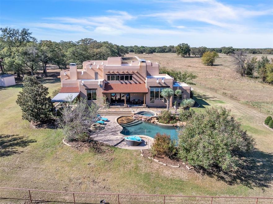 This exceptional custom Santa Fe-style home in Decatur, Texas, offers unparalleled privacy and luxurious amenities on 2 pristine fenced acres. This property combines seclusion with your closest neighbors a half a mile away with the convenience of being just 10 minutes from shopping and local attractions. Outdoors, relax in your private oasis featuring a resort-like backyard complete with lush landscaping, a sparkling pool and spa, waterfall, and an outdoor kitchen outfitted with a Big Green Egg, gas grill, ice maker, drink cooler, and kegerator. Step inside, and you’re greeted by the soaring 20-foot ceilings in the great room, paired with a fireplace and floor-to-ceiling windows, creating a striking entry. Unique design elements, including stained concrete floors, lend warmth and character throughout. The kitchen is a chef’s delight, featuring a gas stove, double ovens, a high-end refrigerator, and a generously sized island, ideal for entertaining. Adjacent to the kitchen, a cozy eat-in breakfast area offers serene views of the surrounding landscape. There's also a wet bar and an elegant dining room anchored by a two-way wood-burning fireplace, perfect for intimate gatherings. The spacious primary suite is a luxurious haven, complete with his-and-hers closets, dual sinks, and a personal vanity. The home also offers a library, media room, and additional bedrooms, each with its own en-suite bath. The finished basement includes a safe room or gun room behind a secure metal door, adding an extra layer of peace of mind. This property is a rare find, a perfect blend of tranquility and luxury. You must see this one-of-a-kind property in person!