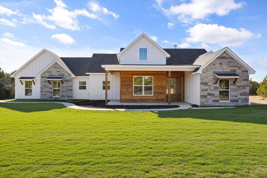 Discover luxurious country living in this stunning new-build home set on 2 serene acres, thoughtfully designed with upscale finishes and custom details throughout. From the moment you walk in, you’ll feel the craftsmanship—soaring ceilings, an open-concept layout, and an elegant flow that blends modern style with timeless warmth. The gourmet kitchen offers abundant counter space, beautiful cabinetry, under-cabinet lighting, and a layout made for both everyday living and effortless entertaining. The living area is spacious and inviting, surrounded by windows that frame the peaceful acreage outside. Retreat to the luxurious primary suite, where relaxation takes center stage. The spa-inspired bathroom features a show stopping walk-in shower with teak wood accents on the ceiling, creating a warm, natural, resort-like feel. Thoughtful touches, elevated materials, and high-end design make this suite a true sanctuary. With 2 acres to call your own, the possibilities are endless—build a workshop or simply enjoy the quiet beauty around you with a seasonal pond. Ideally located approximately 20 minutes to Granbury or Stephenville, you can enjoy the privacy of country living without sacrificing convenience. Located in the desirable Mountain Lakes community, you’ll also enjoy access to two private lakes, a community pool, and more. A rare blend of luxury, craftsmanship, and space—this home is ready to welcome you.