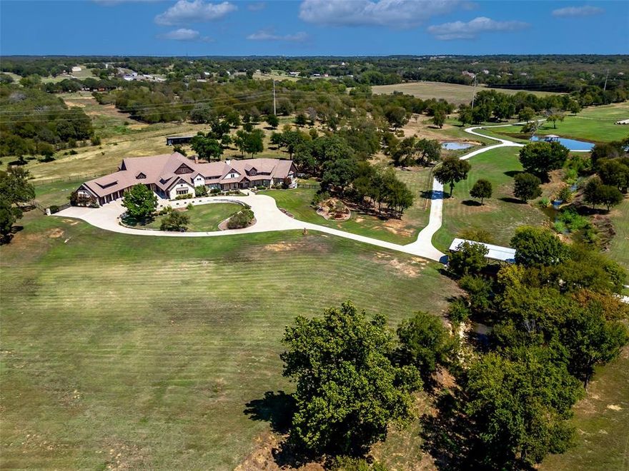 Set on 42 scenic acres in North Texas horse country, this landmark estate blends luxury living, functional improvements, and long-term positioning along the W Sherman Drive (FM 428) corridor between Denton and Aubrey. The custom stone and cedar home offers over 9,000 sq ft of single-story living space with marble and wood flooring, beamed cathedral ceilings, and three fireplaces. The kitchen features premium appliances, gas cooking, double ovens, an island, a butler’s pantry, and a breakfast area, while the formal dining room is anchored by a stone fireplace. The primary suite includes a fireplace, sitting area, private office, a large custom closet, and a spa-style bath with dual vanities, a jetted tub, and a walk-through shower. Additional spaces include a media room, a bonus room, a safe room, and a full recreation wing with a large exercise area, a sauna, a steam shower-equipped bath, and an indoor racquetball court. Garage capacity for up to 10 vehicles plus a Cummins whole-home generator. Outdoor living features a fenced backyard, covered patio with a fireplace, built-in grill, and heated pool with a waterfall. A climate-controlled dog room adds convenience and comfort for your pets. The acreage includes open pasture, mature trees, three ponds, and a creek, making it suitable for recreation or livestock. Equestrian improvements include a barn with four oversized stalls and pipe runs, tack and feed areas, wash rack, lounge with bath, round pen, and fenced pastures. A 60x80 heated and insulated building with six overhead doors, RV hookup, storage, and air system connects to the barn by breezeway. Additional improvements include a 40x46 insulated building with a covered extension and a 32x60 workshop, providing flexibility for equipment, storage, or hobby use. Convenient to Denton, Frisco, major DFW corridors, and airports, with added long-term upside from proposed frontage along the planned Denton County Outer Loop.