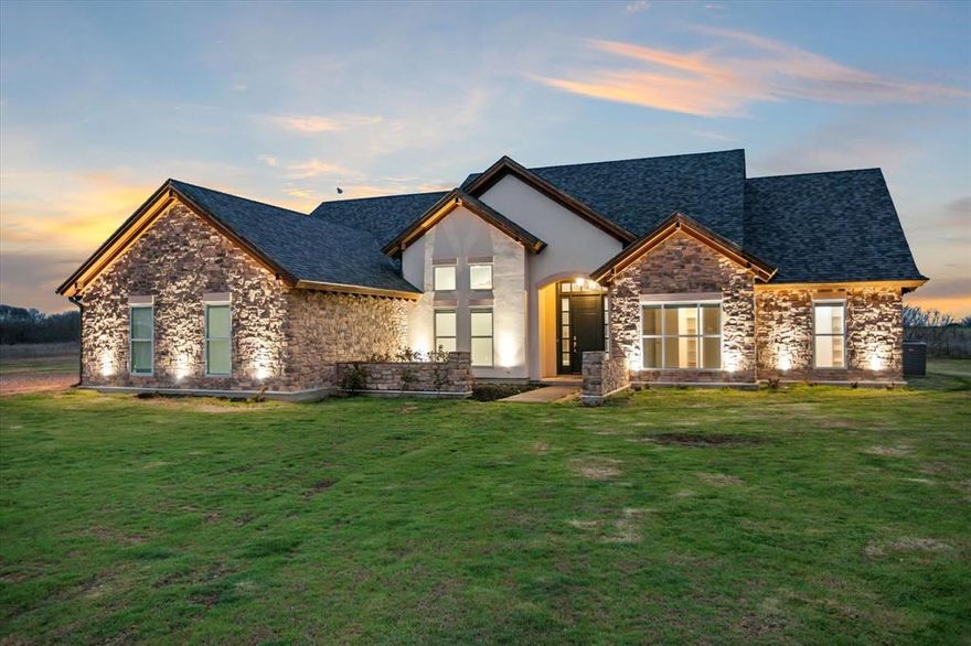 Country home for sale on 4+ acres in Maypearl TX in Ellis County, located minutes from FM 66, FM 916, and an easy drive to Waxahachie, Midlothian, and the Dallas-Fort Worth area. This custom rock and stone ranch-style home offers 4 bedrooms, 3 baths, and approximately 3,022 sq ft designed for comfort and countryside living. Expansive windows capture west-facing Texas sunset views across open pasture, filling the home with natural light. The spacious living area features a stone fireplace, while the primary suite includes its own fireplace, sitting area, and ensuite bath. An open kitchen with breakfast bar, pantry, and built-in cabinetry flows into the dining and living spaces. A large bonus room offers flexibility for a media room, gym, or home office. The 4.27-acre property includes pasture, tank-pond, RV parking, circular drive, and room for shop, animals, or outdoor entertaining. Maypearl acreage home. Ellis County ranch property. North Texas country home near Waxahachie.