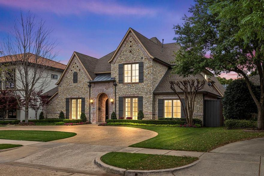 Striking design and effortless livability come together in this Preston Hollow home, ideally located just moments from Preston Hollow Park—one of Dallas’s most scenic and shaded green spaces. A circular drive winds through manicured landscaping to a façade that feels both refined and welcoming. Inside, natural light fills soaring ceilings and highlights a well-balanced layout, with a formal dining room on one side and a dedicated office on the other. A sweeping staircase anchors the entry before the home opens into the main living area, where a stone fireplace, built-in entertainment center, full wall of windows, and integrated Sonos sound system create a space that is equal parts comfortable and elevated.
The kitchen is thoughtfully updated with new quartz countertops, white cabinetry, a center island, and stainless steel appliances, including a JennAir 6-burner gas cooktop and double ovens—designed for both everyday use and easy entertaining. The main-level primary suite offers a private retreat with direct backyard access. Its ensuite features a chandelier, soaking tub, separate vanities, walk-in shower, and whole-home water filtration system. A secondary bedroom on the first floor adds flexibility for guests or multigenerational living. Upstairs includes a game room, media room, exercise room, two additional bedrooms, and a balcony overlooking the backyard. Outside, a covered patio with gas hookup overlooks a saltwater pool and spa with safety fence, all set within a fully turfed backyard (March 2026). The yard is also plumbed for a future fire pit. Exterior Sonos speakers and front and rear security cameras add convenience and peace of mind. Additional updates include a new roof (2025), new hardwood flooring, new carpet in secondary bedrooms, and fresh paint throughout.