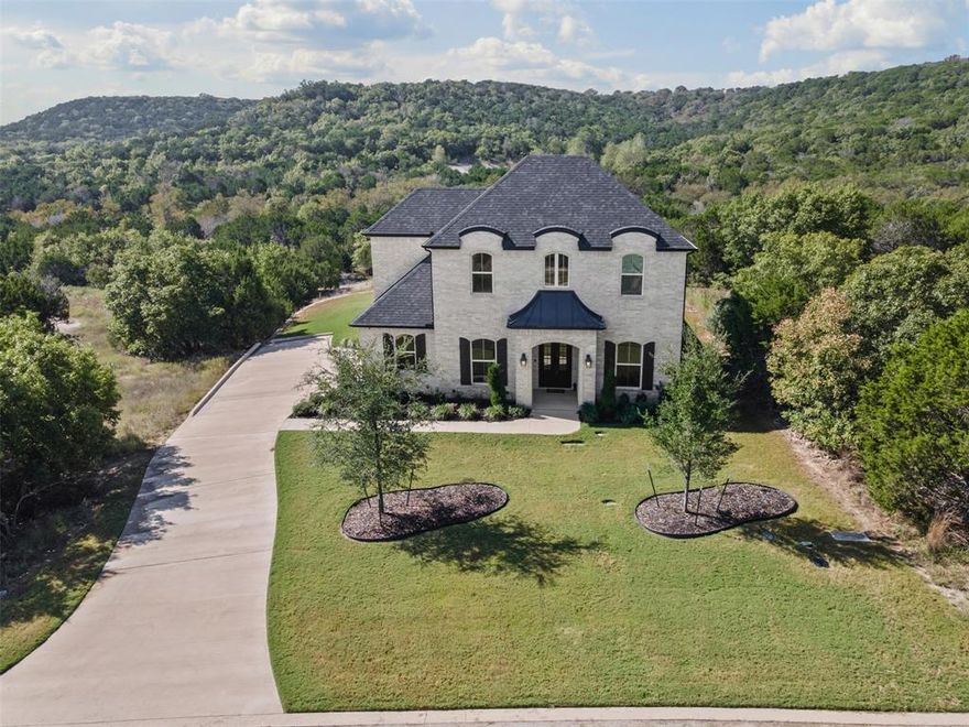 Nestled in the heart of Cleburne, TX, this custom-built French-style residence epitomizes luxury living with its sophisticated design and meticulous attention to detail. Boasting 4 bedrooms and 3 baths, this elegant home combines classic charm with modern conveniences.
Step inside to discover a kitchen designed for culinary perfection, featuring granite countertops, a large island, and soft-close cabinets and drawers. The living room offers a cozy atmosphere enhanced by an electric-start fireplace and a state-of-the-art surround sound system that extends to the primary suite, back patio, and upstairs room. The primary bedroom is a haven of relaxation with ample space and a private bath featuring frameless shower doors. A dedicated reading room with built-in bookshelves invites you to unwind with your favorite novels, while upstairs, the carpet is specifically chosen for its water, stain, and pet-proof qualities. A custom-built office desk with shelves provides a functional workspace, making this home ideal for both relaxation and productivity. The media room elevates entertainment with a fully equipped wet bar, complete with a dual-temperature beer and wine cooler, ensuring the perfect pour every time. Stainless steel appliances and modern touches throughout the home integrate seamlessly for a sophisticated lifestyle. Step outside to enjoy the oversized back patio, where you can immerse in the tranquility of breathtaking views and privacy. The exterior of the home features custom iron French doors and white and grayish painted brick, while the landscape boasts a drought-resistant lawn, maintained effortlessly by a Rain Bird sprinkler system. An oversized 2-car garage complements the design, offering ample storage space. Security and efficiency are prioritized with a whole-home security system and tankless water heater. This residence is a sanctuary of style, comfort, and unmatched luxury, offering a unique opportunity to experience the finest in Cleburne living.