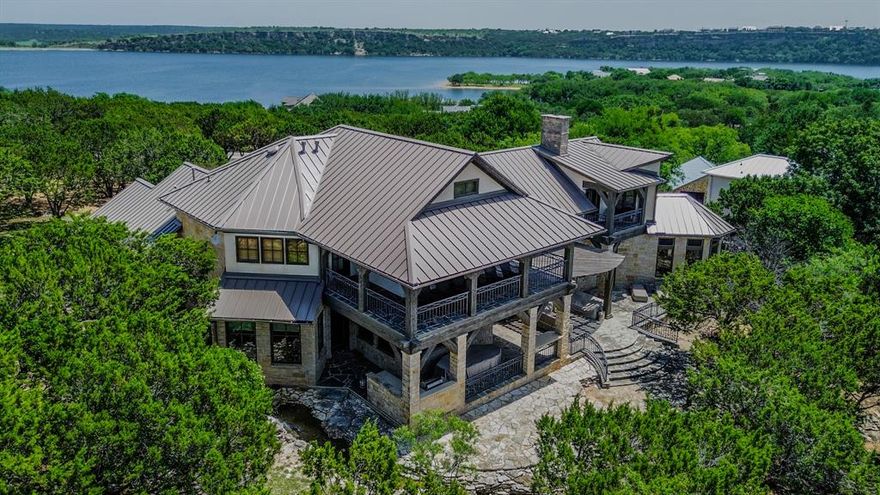 A unique estate is where architecture, ranch and lake resort living come together, creating the lakefront experience that feels as uniquely Texan as it is refined. Located in The Ranch at Possum Kingdom Lake, this main body waterfront estate sits on 1.4+ private acres, paired with access to over 1,100 acres of diverse typography ranch land. But what truly sets it apart is how the property meets the water. A canopy of mature trees surrounds the home, creating a sense of privacy that’s rare on the main body. From there, a custom water feature begins its descent, cascading through stones, winding its way down to a limestone-lined boulder shoreline, blending architecture and landscape into something that feels organic, intentional, and unforgettable. The home itself rises above it all. Expansive observation balconies offer a commanding vantage point of the huge open lake vistas, while below, natural aesthetics of terraced rock patios and covered outdoor living spaces create multiple layers for gathering, relaxing, and entertaining. Inside, the scale matches the setting... soaring ceilings, exposed beams, dramatic stonework, and walls of glass that keep nature in constant view. With over 5,200 square feet, multiple living areas, a game room, and five private bedroom suites, the home is built to host without compromise. The primary suite offers a private retreat with patio access, a spacious bath, and a discreet built-in safe room. Thoughtful systems throughout make ownership easy, whether for weekends or extended stays. Beyond your private lakefront estate, this lake resort community offers over 1,100 acres of shared ranch land, rolling terrain, mountain tops, and open space prairies with guard gated security.  The centerpiece is the organic swimming oasis, a swimming pool that mimics a self-sustaining ecosystem next to courtesy boat slips and launch. Other close by amenities to enjoy are a first-class marina, equestrian facility and lakeside restaurant.