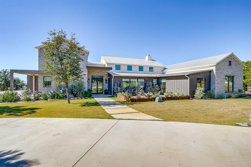 This stunning Modern Hill Country masterpiece is a true work of art, thoughtfully designed to offer luxury and comfort at every turn. Situated at the end of a quiet cul-de-sac, the home boasts sweeping panoramic views, xeriscaping, and a circular drive. Guests are greeted by a welcoming outdoor courtyard, featuring accent lighting that highlights the stone entry wall.
Step inside the open living area, where soaring ceilings, exposed wood beams, and intricate stone accents create an inviting, upscale atmosphere. Natural light pours in through expansive picture windows, bathing the space in warmth. The gourmet kitchen is equipped with top-of-the-line appliances, a convenient pot filler, a butler’s pantry, and a spacious soapstone island.
The primary suite offers an oasis of relaxation, with a stone accent wall and expansive windows that frame breathtaking views. The secondary bedrooms are thoughtfully designed to share a cozy office nook, complete with built-in cabinetry and a dedicated desk space.
Upstairs, a versatile home office and a bonus room provide ample space for work or play. The laundry area offers practical features, including easy access to the fenced dog run, a dog door, and custom cabinetry designed to accommodate pet crates.
This home also boasts energy-efficient spray foam insulation and a built-in storm shelter, ensuring both comfort and peace of mind.