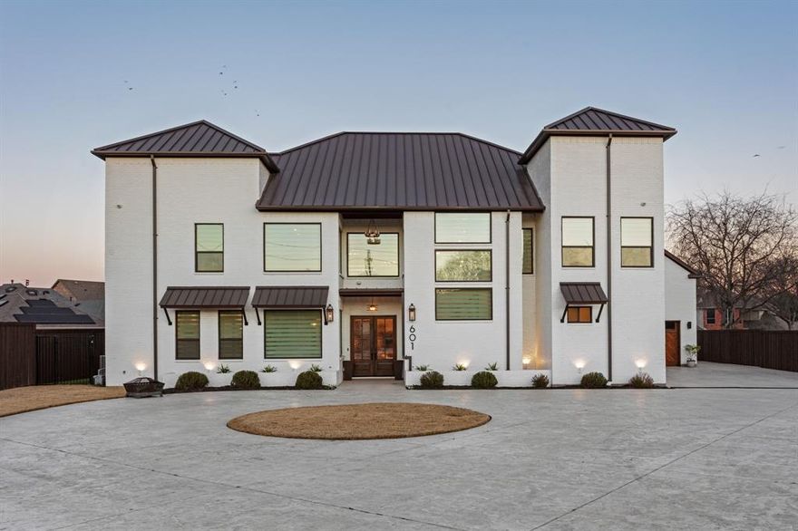 This exceptional custom estate blends architectural sophistication, refined finishes, and modern smart-home technology across a stunning main residence and an expansive guest home. A circular stamped-concrete drive, covered entries, and eight-foot cedar fencing create striking curb appeal and privacy from the moment you arrive. Inside, hand-laid 5-inch white oak hardwoods, soaring 28-foot vaulted ceilings, and an Austin White stone gas fireplace set the tone for elevated living. Entertain effortlessly with a quartz-topped bar beneath the back staircase, a statement dining room with shiplap accent wall and Taj Majal quartzite coffee bar, and a chef’s kitchen featuring an oversized Cristallo quartzite island, pot filler, and professional-grade appliances. The spa-inspired owner’s retreat offers marble finishes, a rainfall shower, and a custom walk-in closet with center island, while secondary bedrooms provide private baths, walk-in closets, and 10-foot ceilings. A private theater with concealed entry, dedicated office, and designer laundry room add both luxury and functionality. Outdoors, enjoy a professionally designed backyard with premium turf, basketball court, and a covered, ventilated porch complete with dual gas grills, fire pit, and wood-burning chimney, prepped for a future luxury pool. The approximately 2,202 sq. ft. guest house with separate utilities is ideal for multigenerational living or entertaining. Built for performance and peace of mind, the home features an engineered slab foundation, closed-cell foam insulation, hail-resistant metal roof, dual high-efficiency zoned HVAC systems, whole-property Generac generator, tankless water heaters, smart irrigation, EV-ready oversized garage, and integrated smart security. A rare opportunity to own a truly distinguished, resort-style estate where timeless design meets modern innovation.