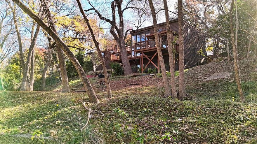 This very unique and special home sits on almost a half-acre cul-de-sac lot in Farmers Branch overlooking the serene Farmers Branch Creek, offering the feeling of a private mountain lodge surrounded by mature trees and peaceful water views. The unassuming curb appeal transforms the moment you enter through the gated entry, where the main level unfolds across an expansive deck. To the left is the inviting entrance to the home, and to the right is the detached two-car garage with additional space for motorcycles, toys, and storage. Inside, the main level features a warm family room with a fireplace and a dramatic floor-to-ceiling wall of windows framing the impressive backyard and creek. One of the primary bedrooms with its ensuite bath is conveniently located on this level. The second floor includes a second primary bedroom, a guest bedroom, and a flex room that can serve as an additional bedroom or office, as well as a loft that delivers incredible panoramic views of the lot and creek—an inspiring spot for work, relaxation, or reading.  The lower level offers a large gameroom and an additional bedroom, ideal for guests or multigenerational living. The expansive wood deck provides outstanding space for entertaining while taking in the spectacular views. The generous half-acre lot gently slopes toward the creek and boasts mature trees, and plenty of grassy area for play. The detached garage also includes a second-level storage space and has the potential to be reconfigured for car enthusiasts, with high ceilings that can easily accommodate car lifts for four or more vehicles. This one-of-a-kind property is moments from 635 and 35 yet feels worlds away, offering the rare blend of convenience and a true escape to nature.