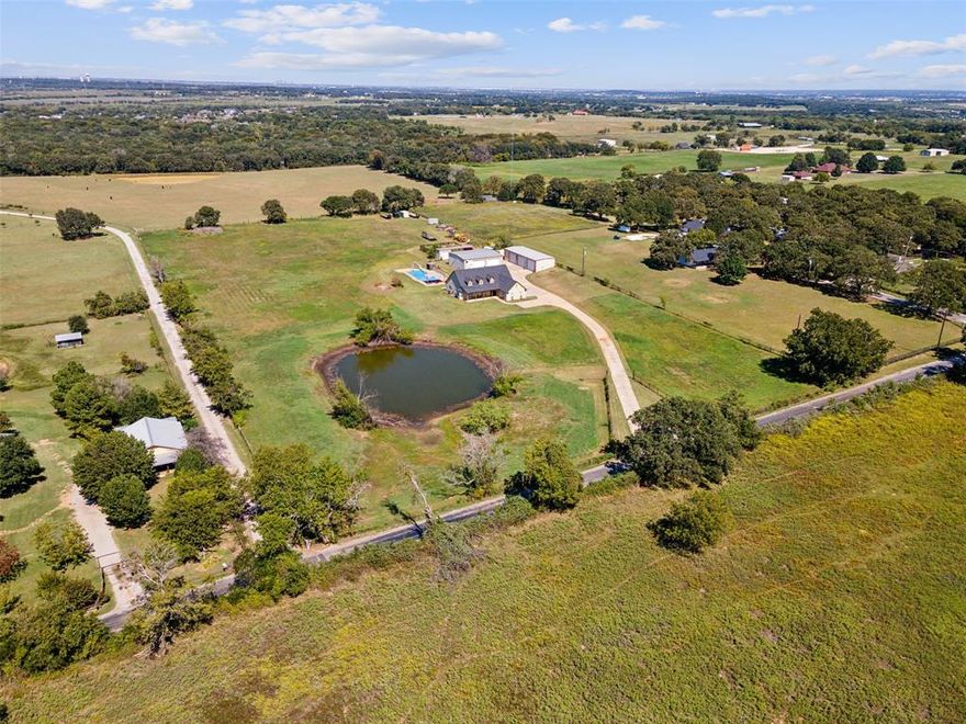 On over 7 acres of serene countryside, this fully fenced property offers privacy, space, and all you need for projects, toys or a business. A spring-fed pond enhances the setting as you enter the property, while the Prairie-style home sits atop the long driveway. The home offers a warm welcome with its open floor plan. Tile floors span the home, and plantation shutters let the light in. With 3 bedrooms and 2.5 baths the well-planned layout is comfortable. The third bedroom, currently used as an office, features a built-in Murphy bed for added functionality. The heart of the home is the kitchen, which opens to the living room with 19-foot ceilings and custom cabinetry. The kitchen is equipped with a large built-in pantry which is almost hidden and adds great storage. For those who value storage and workspace, the property features two large shops. The first, approximately 2,000 square feet is 70x26, includes six car bays and a 200-amp service, perfect for automotive projects. The second shop, measuring 50x40, is equally impressive with an air-conditioned craft room, workout room, bathroom, and laundry space with stackable washer and dryer. A second-level deck adds versatility.
Outdoor living is highlighted by a large, 20x50 diving pool with a 10-foot depth. Additionally, a storm shelter is positioned perfectly on the property for access and safety. Tucked out of sight is a dog pen with an 18-inch footer and high fence. The home is connected to city water with the additional benefit of a 660-foot depth well. The home has spray foam insulation and was painted with Rhino Shield in 2023. There is a new roof and gutters. The house is equipped with a plumbing manifold and two hot water heaters. There is a REME light air purification system. The built-in cabinets in the living area are fitted for a fish tank. This property is a blend of country living with modern convenience. Just minutes from the Chisolm Trail and major
