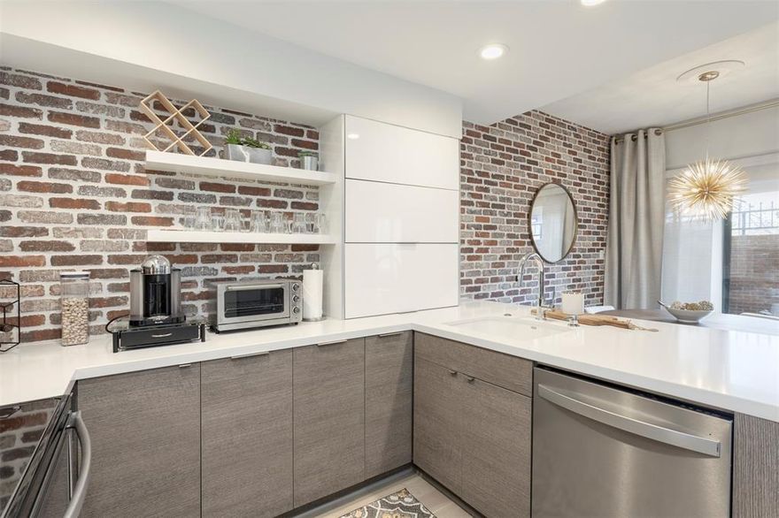 Experience refined living in this exquisitely updated 1-bedroom, 1.5-bath residence located in the coveted Boardwalk on the Parkway community. Positioned on the first floor, this sophisticated condominium offers 985 square feet of curated interiors where timeless comfort meets modern design.
The chef-inspired kitchen is a true showpiece, featuring custom cabinetry including horizontal bifold cabinets, dramatic waterfall-edge countertops at the peninsula, and a striking brick-style backsplash that seamlessly extends into the dining space—creating a cohesive, high-end aesthetic. Thoughtful details continue with modern barn-style doors concealing the pantry and stackable washer and dryer, blending function with architectural interest. The living area exudes warmth and elegance, anchored by a wood-burning fireplace and enhanced by built-in shelving, a wet bar, dual pane low-e windows and abundant storage—ideal for both intimate evenings and elevated entertaining. Step outside to your private, fenced patio, a serene retreat perfect for morning espresso or evening wine. Residents enjoy access to a sparkling community pool, manicured grounds, and the convenience of an enclosed carport with additional storage. Ideally situated in North Dallas near premier shopping, dining, and major highways, this home delivers a lock-and-leave lifestyle without sacrificing sophistication, comfort, or location.