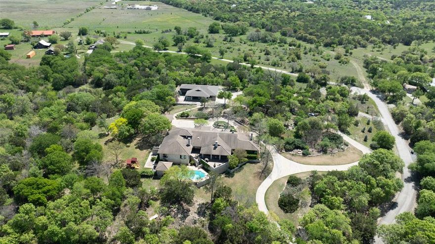 This single-level estate offers an exceptional blend of timeless design and modern luxury on one of Aledo’s most coveted and private streets. The home is filled with natural light, featuring three wood-burning fireplaces, a concrete tile roof, brand-new windows, and a primary suite with its own fireplace, private study, and spa-style bath. Flooring throughout combines wood and carpet for warmth and style. Outdoor living is unmatched with a resort-style pool and cabana, patios, multiple seating areas, and a pool house with a bathroom and storage. A separate 2,700 sq ft guest house includes a full kitchen, laundry, wine room, full bath, and 4-car carport, perfect for multi-generational living or hosting. The property also includes an upgraded water system with Trinity and Paluxy water wells, and abundant storage. Set on 8.77 acres this estate combines privacy, thoughtful architecture, and luxury living in the Aledo acclaimed school district.