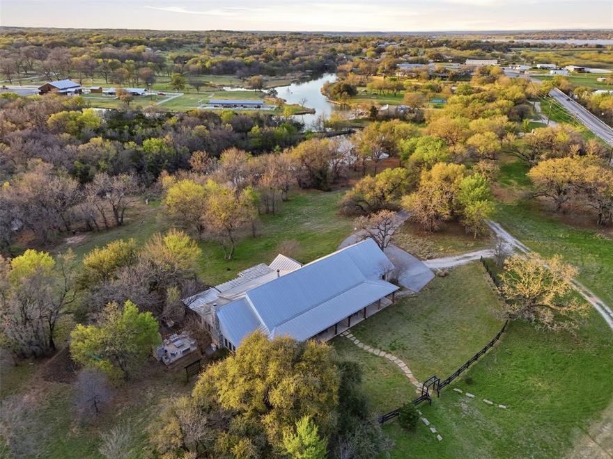 Tucked away on 21 pristine acres along a private stretch of Lake Granbury, this exceptional Texas Modern Farmhouse delivers the ultimate blend of luxury, land, and lifestyle. A long, tree-lined approach opens to a beautifully designed single-story residence with expansive porches, a standing seam metal roof, and timeless architectural appeal. Inside, the home is warm yet refined—featuring vaulted, wood-paneled ceilings, custom millwork, built-ins, and a stunning fireplace anchoring the main living space. The chef inspired kitchen is equally impressive with custom cabinetry, large double islands, high-end gas appliances, and an oversized butler’s pantry with private craft room, designed for effortless entertaining. Coffered ceilings, rich hand scraped hardwood floors, and thoughtfully curated finishes elevate every room. The private primary suite offers a true retreat with serene views and direct outdoor access, while additional living spaces provide flexibility for guests, work, or recreation. Step outside and experience what sets this property apart, multiple outdoor living areas including a covered wrap around patio, pergola, screened-in porch, and a striking stone fireplace gathering space. Overlooking the water and mature trees, every angle invites you to slow down and stay awhile. The land itself is a rare find, rolling pasture, scattered hardwoods, and a peaceful private lake setting complete with dock access. Ideal for recreation, livestock, or simply enjoying wide-open Texas skies. A metal insulated shop with electric, and ample space for expansion add to the property’s versatility. Whether you’re seeking a full-time residence, weekend retreat, or legacy property, this is a one-of-a-kind opportunity to own a private piece of Texas with unmatched character and setting. Private lake frontage of this caliber is rarely available. A true legacy property offering unmatched privacy, natural beauty, and refined living, just minutes from town yet worlds away.
