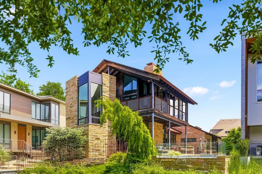 Extraordinary custom modern by Marek Architecture in the acclaimed Urban Reserve community, one of Dallas’ premier eco-conscious architectural enclaves. Perfectly positioned overlooking a tranquil pond, this one-of-a-kind residence blends reclaimed woods, Tennessee Crab Orchard stone, expansive glass, and intentional natural light to create a seamless connection between art and nature. Dramatic pivot entry opens to sophisticated interiors with wood-burning fireplace, chef’s kitchen with premium appliances, and exceptional indoor-outdoor living spaces. Flexible upper level offers ideal setup for dual offices, guest retreat, or creative studio, complete with coffee bar and screened porch featuring see-through fireplace. Stunning primary suite features spa-inspired bath with soaking tub framed by reclaimed wood paneling. Resort-style pool and spa overlooking the water, fully equipped outdoor kitchen, fire pit, covered patios, and lush landscaping create an unparalleled modern retreat unlike anything else in Dallas.