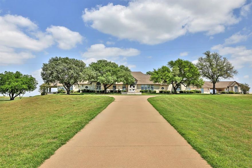 This exclusive 12.6-acre lakefront estate on Lake Cleburne offers luxurious single-story living with a blend of elegance, comfort, and privacy. The home welcomes you with marble and hand-scraped wood floors, and expansive living spaces enhanced by 12-foot ceilings and crystal chandeliers. The main residence features four spacious living areas, a gourmet kitchen with dual ovens and microwaves, granite countertops, and an oversized island. The primary suite includes a marble fireplace, a seating area, a spa-like bath, and a massive custom walk-in closet. Outdoor amenities include a resort-style pool and spa, a gazebo, covered patios with stunning lake views, and a fully fenced yard with two wrought iron electric gates. The property also includes a 5-car garage with a workshop, a tornado shelter, a fireproof safe, a decked attic with a separate stairwell, and a brand-new Class IV roof. Through the porte cochere, the guest quarters offer a full kitchen, living and dining areas, a full bath, and a bedroom with a cedar closet. Most of the high-end furnishings are included in the sale, making this a move-in-ready retreat unlike any other.