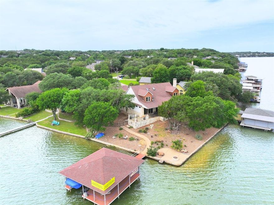This one is a stunner. This main body lakefront home shines with style and distinction. Designed to bring in the view with a wall of windows overlooking the waterfront, the spacious open concept floor plan features a huge family room with vaulted and beamed ceilings, a stunning rock fireplace, wet bar, and a separate office or library area just off to the side.  The kitchen was designed for hosting, with a commercial grade 6 burner gas range, an expansive island, double ovens, a warming drawer, wine cooler, a kegerator and semi-precious LABRADORITE stone countertops that are enhanced by the blue in the cabinets and will take your breath away.   The primary suite is downstairs and enjoys a private walk-out porch overlooking the lake. The en suite bath was built to spoil the owners with a steam shower, jetted tub, double vanities and a huge closet—perfect after a long day on the water.
The first floor features a an additional guest bedroom, a second full bath and a powder room for guests. Upstairs you will find two more guest bedrooms and the 3rd full bath.  This one was built to ensure all of your guests are comfortable.  There is a fabulous workspace and utility room just off the kitchen as well as a small solarium ideal for a private reading room or a home gym equipped with a built in Murphy bed ideal for those unexpected last minute extras. Outside is where the magic happens with a covered back porch that spans across the back of the home which is situated on a point with over 150' of frontage on Lake Granbury, you will find a built-in grill, fire pit, a fabulous Boat Dock with an automatic touch-less boat cover, two 360-degree jet ski lifts and a generous sized party deck.