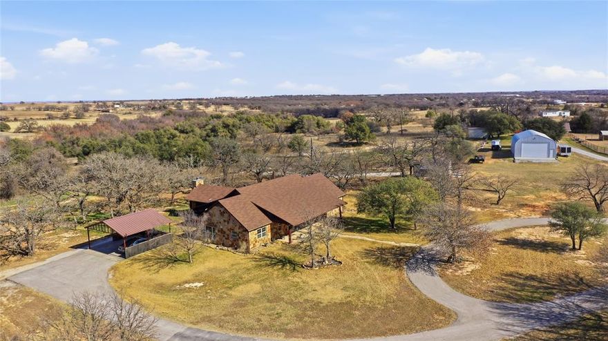 Set beyond a winding drive that meanders through rolling pastures, this breathtaking 40-acre ranch unfolds as a true Texas sanctuary. The custom stone ranch house is thoughtfully positioned to take in the land, wide-open skies, scattered mature trees, and the kind of quiet that lets you exhale the moment you arrive. The heart of the home is a stunning updated kitchen anchored by a massive taj mahal quartzite island & copper farmhouse sink, flowing seamlessly into a spacious dining area with a recessed ceiling & wood-burning stove. The living area & open office space continue creating a warm, connected layout filled with natural light. A generous game room offers flexible space for hobbies, fitness, or gatherings. The primary suite is a private retreat with a serene, spa-like bath & a custom closet featuring a private vanity. 2 guest rooms on the main level share a Hollywood bath, while a fourth bedroom upstairs functions beautifully as a secluded guest suite with its own ensuite bath. Throughout the home, custom western metal lighting, incredible custom cabinetry, fabulous wood doors, cowhide transoms, & branded trim add distinctive character & craftsmanship to this home. Incredible outdoor living area, with stone wood-burning fireplace, vaulted ceiling, & spa, overlooks the backyard & surrounding trees, creating a natural extension of the home and an ideal spot for morning coffee & evenings under the stars. The property is complete with a 30x50 insulated shop w electricity, great for parking all your toys! 2well houses w implement parking & storage. 2 stall shedrow. The older BarnMaster, currently used as a workshop & feed room, was once a 2nd residence as it features a kitchen & bath needing TLC. Wooded trails & the gorgeous stock tank invite exploration. Lush coastal Bermuda grass. Private, peaceful, & beautifully positioned, this remarkable ranch offers the best of country living, just 31 miles from downtown Fort Worth & 52 miles from DFW International Airport.