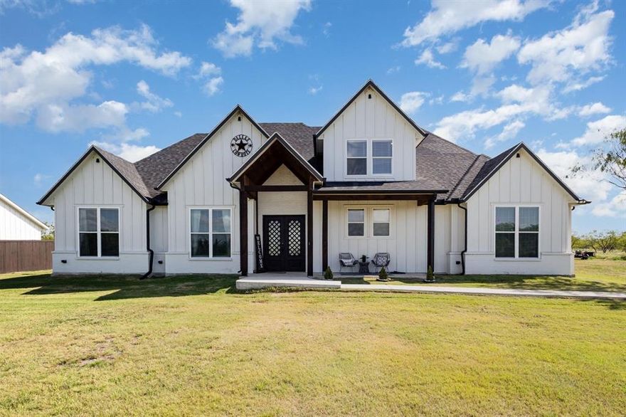 601 Gin Road in Ennis, Texas, is a beautifully designed modern farmhouse set on 3.75 serene acres, just 45 minutes south of Dallas. Built in 2023, this 4-bedroom, 3-bathroom home offers 2,649 square feet of open-concept living with vaulted ceilings, exposed cedar beams, and luxury vinyl plank flooring throughout. The heart of the home features a spacious great room with a wood-burning fireplace and a chef’s kitchen complete with quartz countertops, custom cabinetry, a gas cooktop, and a double farmhouse sink. The main-level primary suite offers a spa-inspired bathroom with a freestanding tub inside a walk-in shower and dual vanities. Two guest bedrooms and a full bath are also located on the first floor, while upstairs includes a fourth bedroom, a full bath, and a loft-style media room. Energy-efficient spray-foam insulation keeps the home comfortable year-round. Outside, the property includes a gated entrance, a horse stall, a chicken coop, and a small pond, offering peaceful views and a perfect setting for relaxed country living.