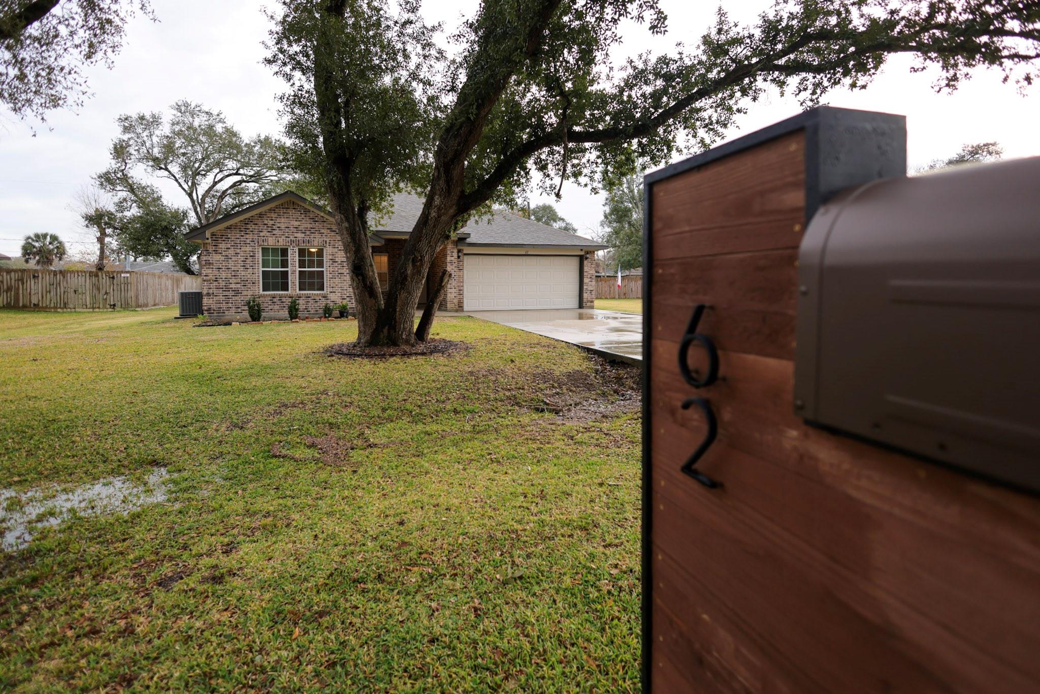 Charming brick home with a spacious front yard, mature trees, and a welcoming driveway leading to a two-car garage.
