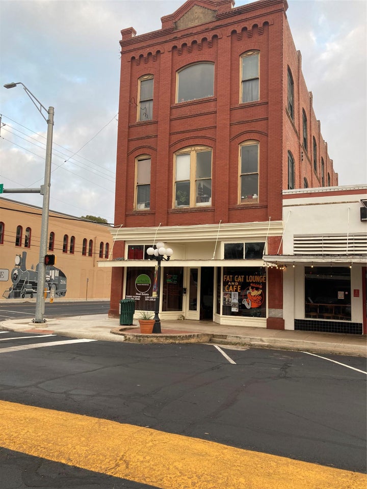 Brick commercial building featuring three stories, multiple arched window openings, a decorative parapet, and…