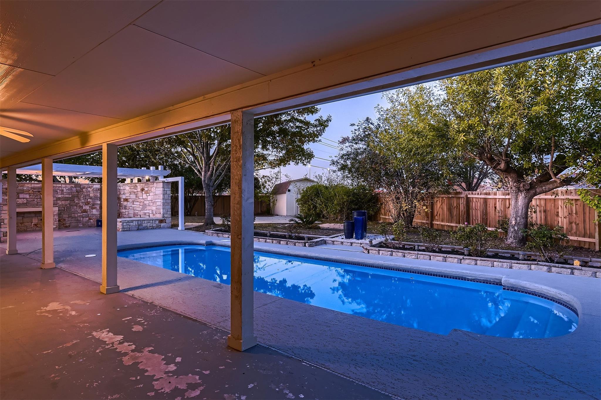 A view of a backyard with a swimming pool, viewed from a covered patio area.