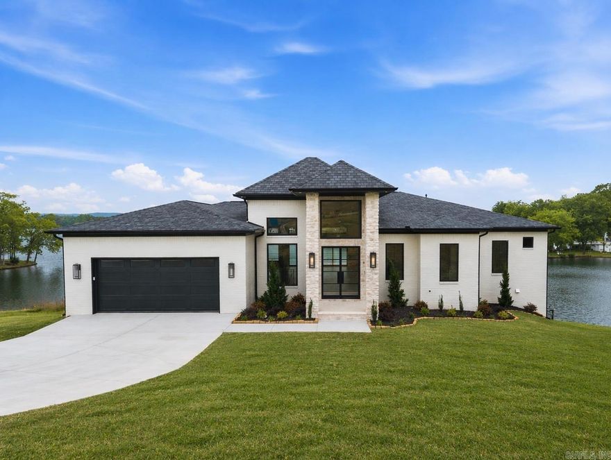 Experience Lake Front Luxury in this brand-new Vista Point showpiece with panoramic Lake Hamilton views, just minutes from Oaklawn and historic Bath House Row. Step through the soaring 16-foot entry into a breathtaking living area where a custom site-built fireplace and quad sliding glass doors frame endless water views and open to a massive covered deck with a gas fire table! The gourmet kitchen is a culinary dream, featuring a professional 6-burner gas range, double oven, built-in refrigerator, wine fridge, waterfall island, and an oversized butler’s pantry. The main-level primary suite offers lake views, a cathedral ceiling, spa-inspired double-sided shower, dual vanities, and a huge walk-in closet with its own washer and dryer. Downstairs, entertain like never before in a full-scale bar with a dramatic wall of liquor and wine shelving, seating for guests, and a spacious game room. A second primary suite, additional laundry, and more deck space complete the lower level. Outdoors, enjoy your private boat dock, full outdoor kitchen, and 3-car garage—all designed to deliver an unforgettable lakeside lifestyle.