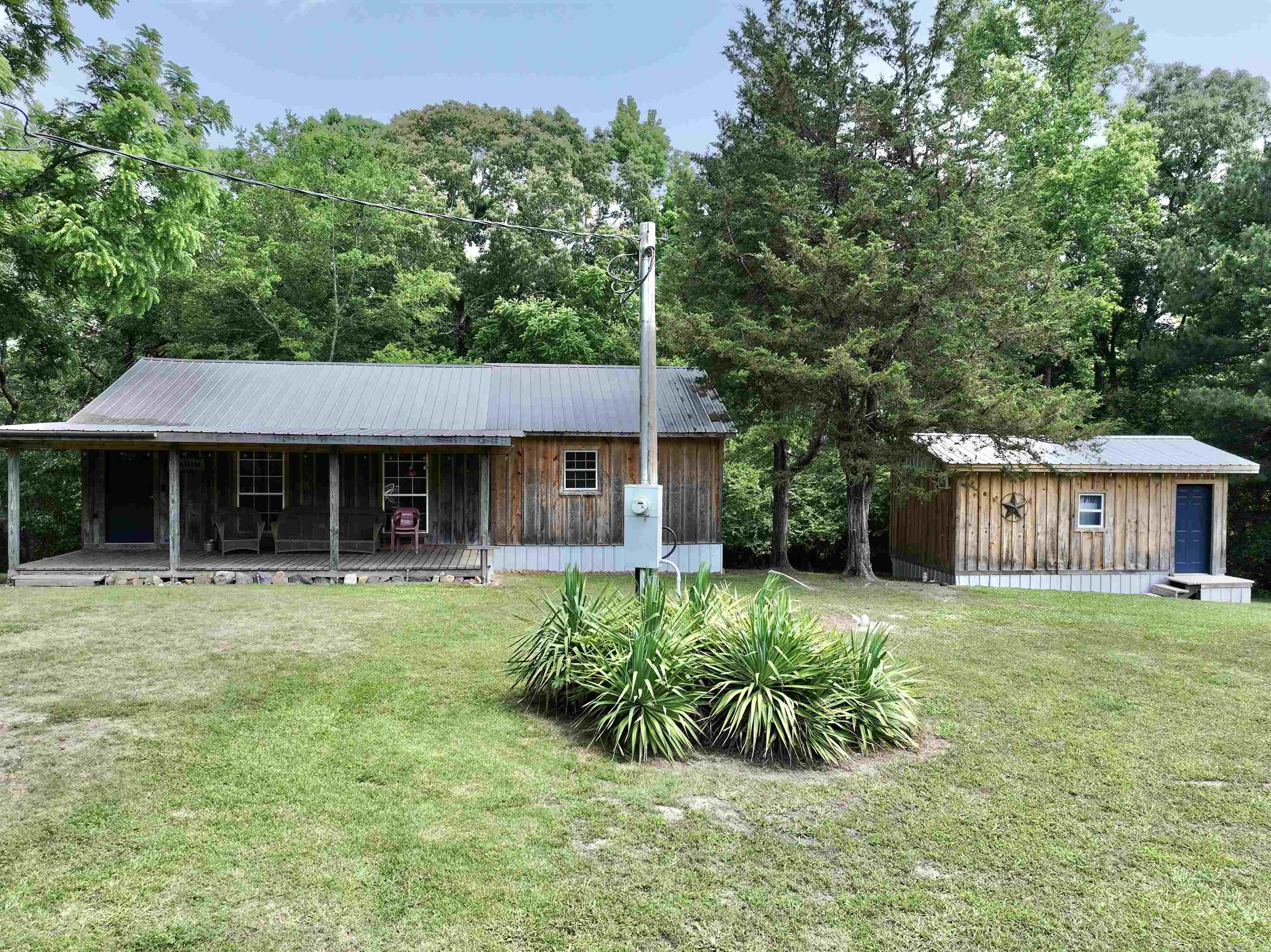 Fantastic opportunity in Rosboro! This charming property spans 3.88 ± acres and includes two cozy cabins (sleeps 12), RV hookups, a picturesque creek, a convenient storage building, and a deck complete with a fun slide for added enjoyment. Nestled in a serene rural setting, it offers the tranquility of country living while being conveniently close to town and the beautiful Caddo River. The main cabin is designed for comfort and relaxation, featuring a generous living area that invites you to unwind. The bedroom provides direct access to a deck, perfect for morning coffee or evening stargazing and a loft for additional lodging. A welcoming front porch adds to the cabin's appeal, offering a peaceful spot for sitting and soaking in the natural surroundings. The additional cabin enhances the property's versatility, offering a comfortable bedroom and a spacious bathroom, making it an ideal guest retreat or rental opportunity. Both cabins blend rustic charm with modern amenities, creating a warm and inviting atmosphere. This property is a perfect blend of convenience, comfort, and rural charm, making it an exceptional find for those seeking a peaceful retreat close to nature.