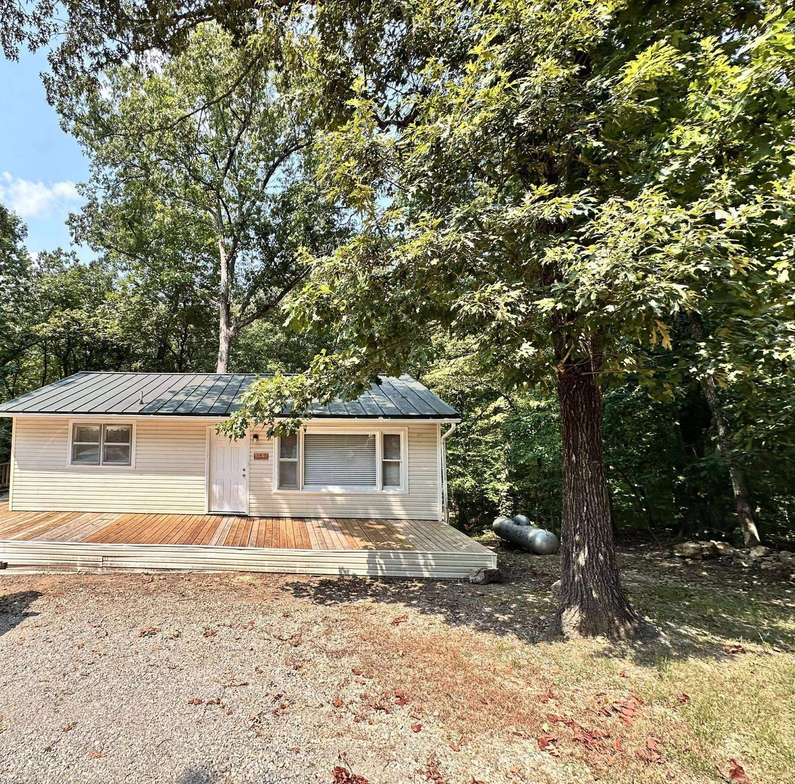 This charming 2 bedroom/1 bath ranch-style home is waiting for you. Step outside and enjoy your morning coffee on the expansive back deck, nestled among the trees and overlooking a peaceful wet weather creek. The inviting wraparound deck offers plenty of space for outdoor living and relaxation. Inside, the home has been thoughtfully renovated to preserve its classic charm, and the kitchen offers a new oven. Window units are sufficient for AC, and there is a gas heater to provide heat for colder months. The spacious walk-out basement is perfect for extra storage, housing everything from recreational gear like kayaks and side-by-sides to your favorite tools on the built-in workbench. The garage door provides easy access, and some cars may fit under the deck and/or inside the basement. Experience comfort and tranquility in this turn-key home, ready for you to move in and make it your own! (wide-angle photography)