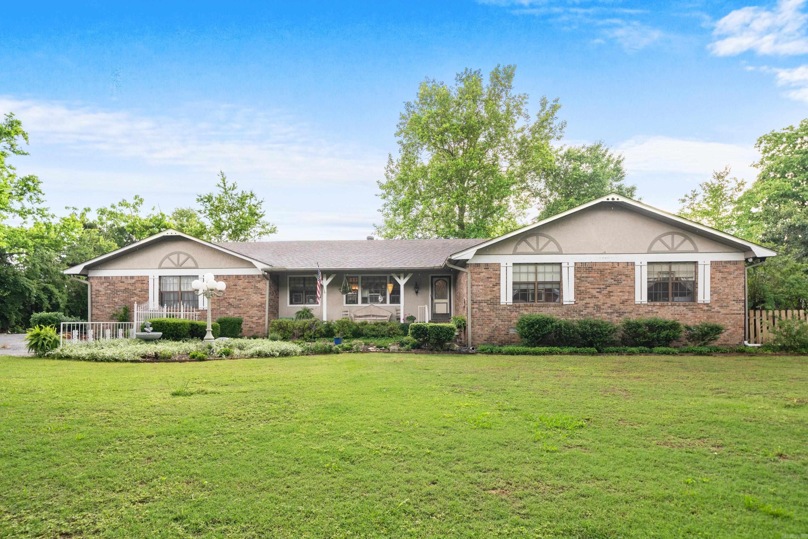 Enjoy privacy and seclusion on 2.9 fully fenced acres within the city limits. Mature cypress trees provide a peaceful, park-like setting. This singel level, 4-bedroom, 4.5-bath home includes en suite bathrooms in every bedroom, a formal dining room, and a spacious hearth area with a wood-burning stove and built-in wood storage-perfect for cozy gatherings. The bonus room, complete with a wet bar and full bath, offers flexible space for a fourth bedroom, home office, or game room. Step outside to a covered patio that invites outdoor living. The property also includes a 24x48 workshop/utility building with four bay doors, an RV hookup with electricity and sewer, and a secure dog run. A rare find that combines space, function, and natural charm—all within the city limits.