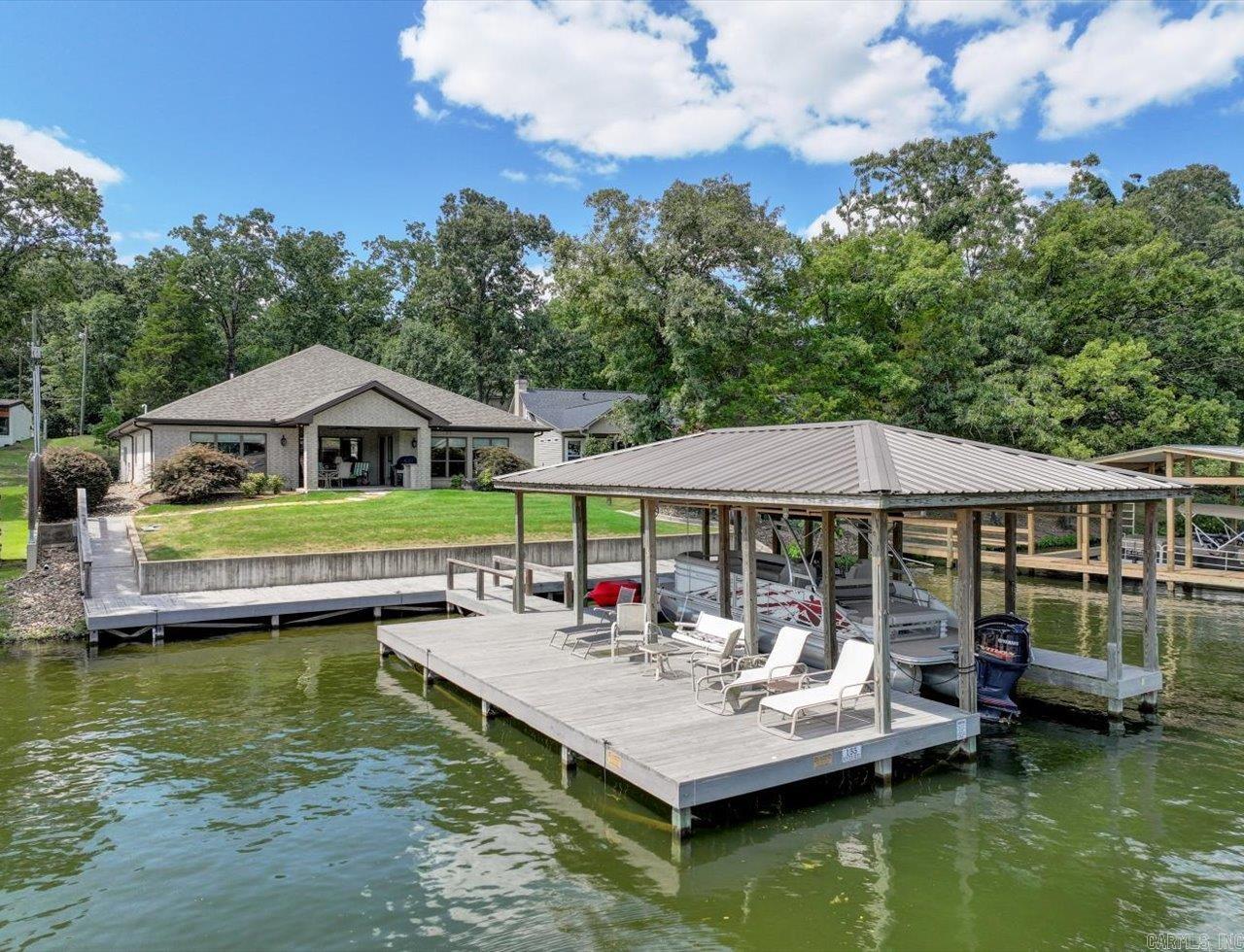 This Lake Hamilton home is a stunning three-bedroom, three and a half bath retreat. Situated on an extra large lot, the property offers ample privacy and space for an RV pad or ADU (Assessory Dwelling Unit). The house boasts a contemporary design with large windows that provide views of the lake. Inside, the open-concept living features high ceilings, a cozy fireplace and stylish finishes. At this point I need to mention the 6" exterior wall construction for maximum strength and insulation. The gourmet kitchen is equipped with modern appliances, beautiful granite countertops and a spacious island. Each bedroom is generously sized with the primary suite offering a luxurious ensuite bathroom with a soaking tub and walk-in shower. The additional two bedrooms also have their own private bathrooms. Outside, the highlight is the very nice fixed boat dock, with lift, which provides easy access to the lake. The patio area is ideal for outdoor cookiing, dining and relaxation, making this home a perfect lakeside getaway. There's a lakewater sprinkler system and a beaitful green lawn. This vacation home has barely been lived in and it shows! It's a pleasure to view this property.