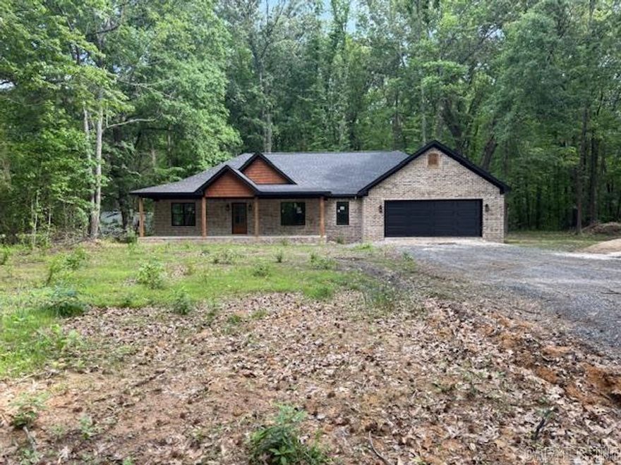 New construction home nestled on a private, wooded lot offering peace, space, and modern style. This thoughtfully designed home features an open-concept layout with a spacious living area, soaring ceilings, and a striking exposed beam. The kitchen is a standout with custom cabinetry, a large island, quartz countertops, and stylish lighting—perfect for entertaining.  The primary suite includes a spa-like bath with a tiled walk-in shower and double vanity. Additional highlights include a dedicated laundry room with built-in cabinetry, generous storage throughout, and a covered front porch ideal for relaxing and enjoying the natural surroundings.  Exterior features a classic brick finish with warm wood accents and a sleek dark garage door for great curb appeal. Located in a quiet setting with no restrictions, giving you the freedom to truly make it your own.