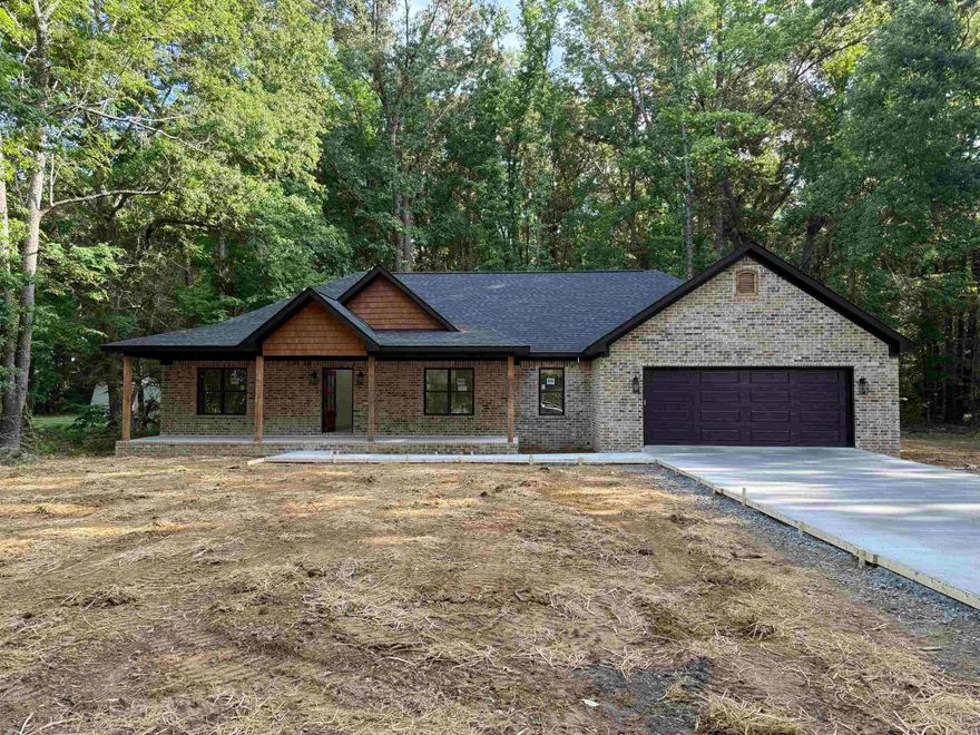New construction home nestled on a private, wooded lot offering peace, space, and modern style. This thoughtfully designed home features an open-concept layout with a spacious living area, soaring ceilings, and a striking exposed beam. The kitchen is a standout with custom cabinetry, a large island, quartz countertops, and stylish lighting—perfect for entertaining.  The primary suite includes a spa-like bath with a tiled walk-in shower and double vanity. Additional highlights include a dedicated laundry room with built-in cabinetry, generous storage throughout, and a covered front porch ideal for relaxing and enjoying the natural surroundings.  Exterior features a classic brick finish with warm wood accents and a sleek dark garage door for great curb appeal. Located in a quiet setting with no restrictions, giving you the freedom to truly make it your own.