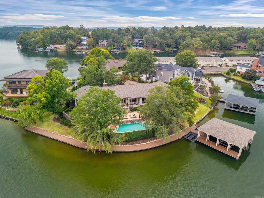 Exquisite Point Property on Lake Hamilton! Welcome to your private paradise on the shores of beautiful Lake Hamilton! This stunning one-level estate is perfectly positioned on an exclusive point offering 289 feet of pristine waterfront and panoramic lake views from nearly every room. Designed for both relaxation and entertaining, this home features an in-ground pool, multiple covered patios, and a private boardwalk with Trex decking leading to a 2-stall stationary boat dock complete with Sea-Doo slips. Inside, you’ll find a spacious open-concept layout boasting 3 bedrooms—each with a private ensuite, 3.5 baths, a dedicated office, and a game room/bunkroom perfect for kids or guests. The chef’s kitchen is a showstopper with stainless appliances, solid surface countertops, ample storage and pantry. Home also features a wet bar, and a temperature-controlled wine refrigerator.  Your primary suite offers the perfect retreat—complete with a spa-inspired bathroom and luxurious STEAM ROOM, creating a true sanctuary for rejuvenation. Additional highlights include hardwood floors, oversized  storage room in the unfinished basement, and encapsulated crawl space for peace of mind.