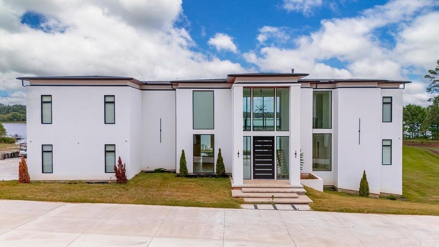 Stunning modern home with floor-to-ceiling glass and panoramic lake views. Open living area with two-story ceilings and dramatic fireplace. Chef's kitchen with premium finishes including Dekton countertops. Floating staircase, pivot doors, clean architectural lines. 25' ceilings in foyer and great room; 12' throughout the rest of the house.  Main level features a private primary suite with fireplace & spa bath, upper level sitting room w/ private deck. A guest bedroom and bath is also located on main level.  Upper level includes two spacious bedrooms, exercise room overlooking the lake, an office, theatre room and a private indoor golf studio. Finished basement bonus room, tornado shelter. Elevator entry (not installed) available from great room. Fully equipped outdoor kitchen, lighted pool w/waterspouts, circular drive, iron fencing around the front. All situated on a little over an acre lot. True resort style living!