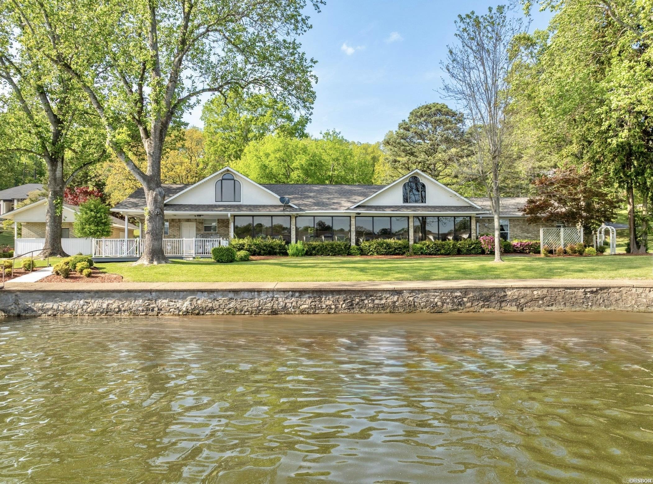 An exceptionally rare find on Lake Hamilton! This expansive Lake Hamilton property spans just under one acre across two beautifully manicured lots and boasts approximately 200 feet of prime lake frontage with year-round water and stunning panoramic views. The main residence is thoughtfully designed with a single-level layout and no steps, offering ease of access throughout. Inside, you'll find 3 spacious bedrooms and 2.5 bathrooms, including a generous primary suite with a private en suite bath. Additional features include an open layout, cozy fireplace, a sunroom, office and large windows framing lake views from nearly every room. A new roof adds peace of mind and lasting value. Also on the property is a charming 300 sq. ft. guest house studio apartment with bath, complete with an attached workshopāperfect for guests, hobbies, or additional rental income. Outdoor living is just as impressive, with impeccably landscaped grounds, a two-car carport, a covered boat slip with lift, and plenty of room to relax or entertain. This is the kind of property that rarely comes availableāoffering privacy, space, and an unbeatable lakeside lifestyle.