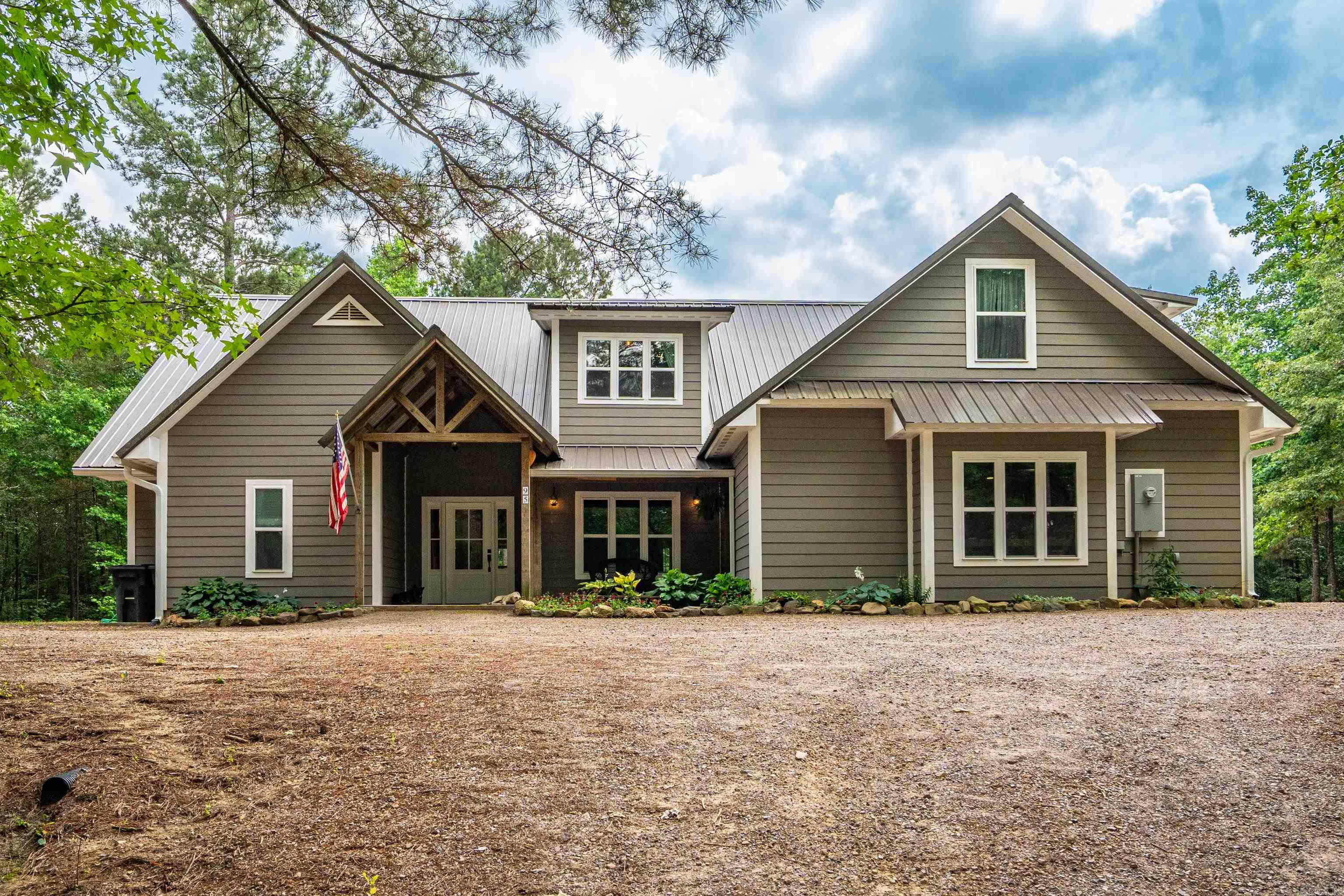 Welcome to 95 Thunder Mountain—a stunning luxury homestead tucked into 7.9 acres of peaceful Caddo Gap wilderness. This custom-built estate includes a beautifully crafted main home and a high-end 2-bedroom guest house, both topped with 50-year metal roofs and designed for energy efficiency. Inside the main home, bamboo floors, vaulted ceilings, and a wood-burning stove set the tone for warmth and charm. Floor-to-ceiling windows bring the outdoors in, flooding the open-concept living, dining, and modern farmhouse kitchen with light. The main level features a spacious primary suite with a clawfoot tub, vintage-style vanity, and walk-in closet, plus a second bedroom for kids or guests. Upstairs offers three more bedrooms, a full bathroom, and a bonus space perfect for a playroom, media room, craft room, or office. It's perfect for large families! The guest house is equally impressive—open, airy, and ideal for multigenerational living or short-term rental income. All of this is just minutes from the Caddo River, Ouachita National Forest, and crystal mines; this is Arkansas luxury homesteading at its finest.