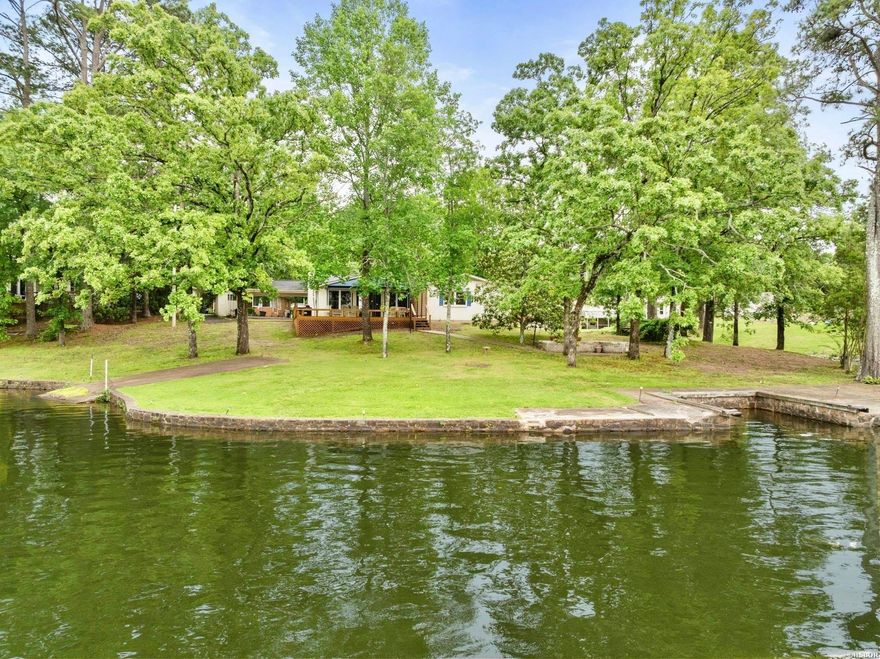 A truly unique opportunity on Lake Hamilton! This beautiful home sits on over half an acre and offers nearly 400 feet of lake frontage, with water wrapping around the property to create breathtaking panoramic views from every angle. The home features 3 bedrooms and 2 bathrooms - all on one level with no steps! The open living area flows seamlessly to a large outdoor deck—perfect for entertaining or relaxing by the lake. Additional highlights include new vinyl plank flooring, woodburning fireplace, newer roof, a two-car carport, two storage buildings for all your lake gear, and even a private boat ramp for easy lake access. Located in the heart of Hot Springs, this property combines convenience with serene lakefront living—just minutes from shopping, dining, and entertainment. Don't miss this rare find with unparalleled lake frontage and endless potential!