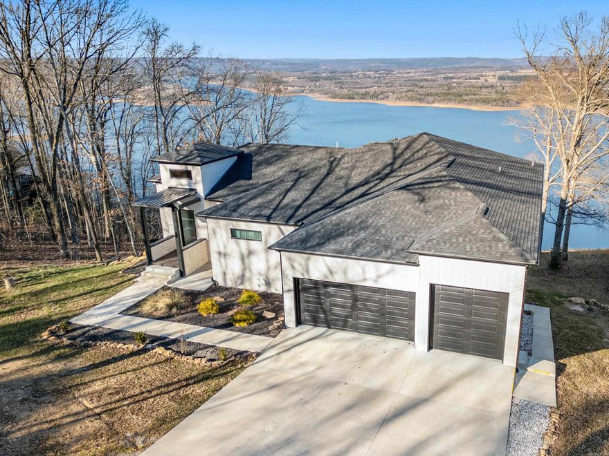 This stunning 2024-built modern luxury home was designed to showcase breathtaking views of Greers Ferry Lake from nearly every room. Offering over 4,700 sq ft, the open floor plan features soaring 12’ ceilings, cloud lighting, and smart-home technology for effortless living. The main living area with gas fireplace flows into the chef’s kitchen with quartzite counters, smart gas range with built-in air fryer, and walk-in pantry—ideal for hosting family & friends. Step onto the covered deck with its own gas fireplace and soak in the lake views. The primary suite offers an electric  fireplace, stunning lake views, spa-like bath with large walk-in tile shower, and a walk-in closet with center island. The main level also includes a guest bedroom, full bath, laundry room and half bath. The lower level features a full kitchen, living area, and two additional bedrooms. An epoxy-finished 1177 sf patio provides another entertaining outdoor space overlooking the lake. A three-car garage, with the third bay perfect for a boat or workspace, completes this remarkable property that blends modern luxury all throughout the home.   A must-see lakefront retreat!
