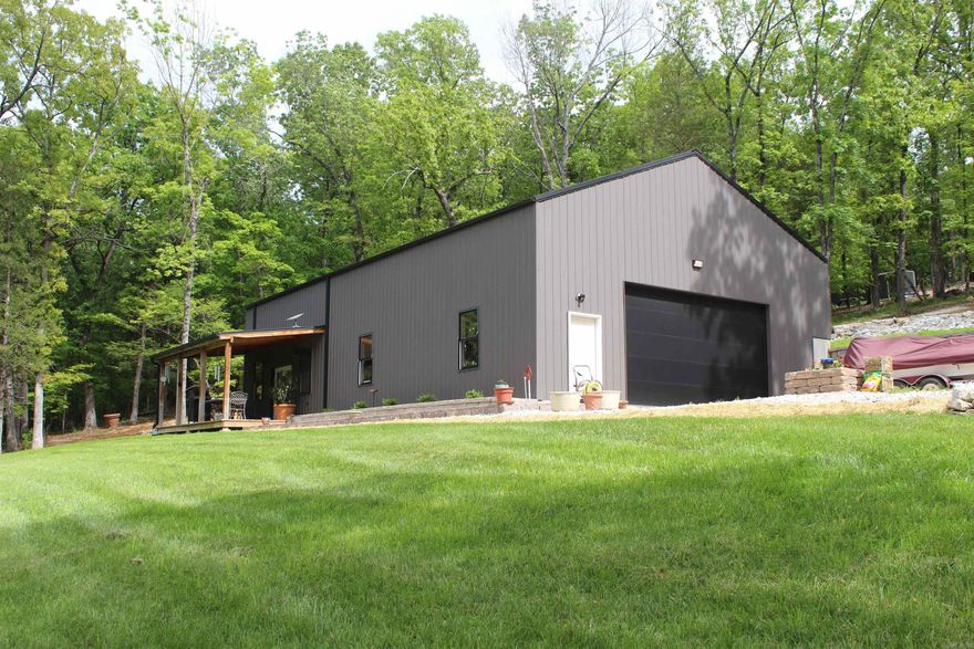 Nestled on 2.73 acres in a gated subdivision, this unique property offers privacy and scenic beauty, bordering Corps of Engineer land on two sides with views of the surrounding landscape and nearby Bull Shoals lake. This 64' x 36' barndominium features a 24' x 36' finished living space and a 40' x 36' fully heated shop with 14-ft walls. The living area showcases a vaulted tongue-and-groove pine ceiling, tile floors, granite countertops, stainless steel appliances, pantry, and spacious closets. A custom tile shower, solid oak 36” interior doors, and oak trim add quality throughout. The loft bedroom provides a cozy retreat, while French doors open to the outdoors. Enjoy the covered deck and landscaped yard. Located in a community with a private airstrip, this property blends comfort, function, and outdoor living and less than 10 miles to boat launch.