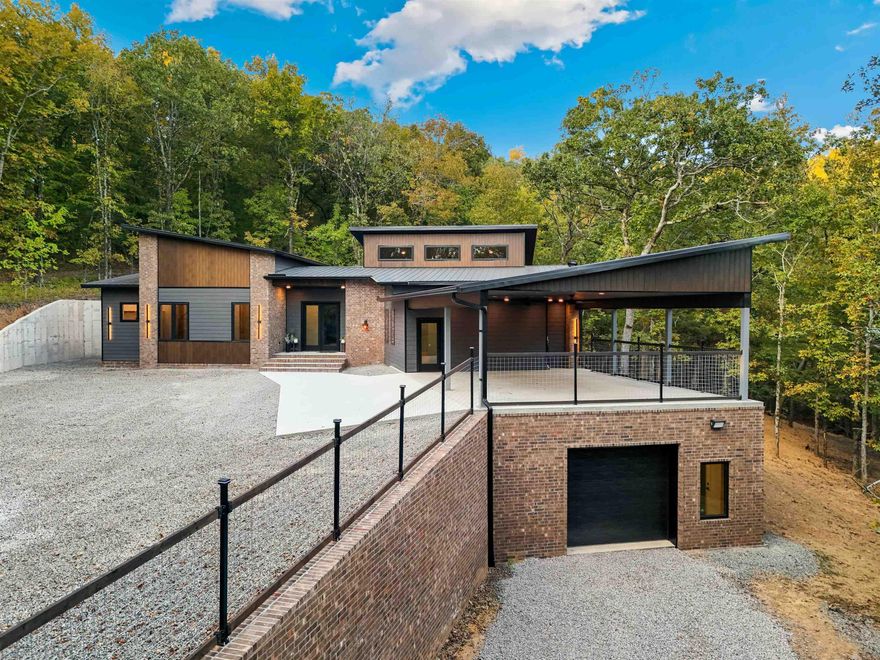 Stunning modern nestled into a hillside among the trees. This gorgeous home is surrounded by woods on all sides, with towering windows that bring natural beauty in to the living spaces. The custom kitchen has a double oven, convection cooktop, eat-in island, and a second sink for prep or coffee station. The living and dining areas are vaulted and surrounded by windows. A half bath is just off the living room. Adjacent to the living area is a fully-insulated media room with built-in ceiling speakers and in-wall subwoofer box. There are two additional flex rooms which can be used for office,  hobby room, or additional bedrooms. The primary suite and junior suite both have an attached full bath and walk-in closet. The 3-car carport is attached and also serves as the roof to the 925sqft heated and cooled basement, which is a safe room and can be accessed from inside and outside the home. Additional features include Anderson casement windows throughout, a highly efficient Rudd HVAC system, instant water heaters, and a car charger. The home is built in the center of 5.47 acres. A wet-weather creek with cascading rock ledges runs to the East of the house. Trails wind around the property.