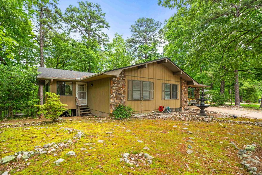 Adorable 2 bedroom house that feels like a treehouse from the den! The Arkansas room offers a second gathering space full of windows for morning coffee or a great craft space. A handy heated & cooled workshop space is available under the house for extra storage or projects.  The living room has classic parquet wood flooring and a grand stone fireplace with electric insert for easy ambiance and additional heat source.  NEW ROOF and NEW HVAC in 2024 gives peace of mind for ease of maintenance  Enjoy the peace and tranquility of Hot Springs Village and its amenities. The lot behind the house is available for purchase as well for added guaranteed privacy.