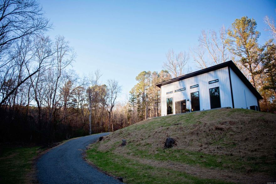 Welcome to this stunning modern retreat nestled in a peaceful, wooded setting. This home is walking distance of the Middle Fork of the Little Red River, with a tranquil natural branch flowing through the front of the property. This thoughtfully designed home features sleek vertical metal siding, a striking mono-pitch roofline, and clean architectural lines that blend beautifully with its natural surroundings.  Inside, you’ll find a bright, open-concept living space with soaring ceilings, sealed concrete floors, and abundant natural light from oversized windows. The designer kitchen showcases custom wood cabinetry, a large center island, stainless steel appliances, and modern pendant lighting—perfect for entertaining or everyday living.  Enjoy seamless indoor-outdoor living with easy access to the surrounding landscape, ideal for morning coffee, evening sunsets, and quiet weekends. Located just a short drive from Greers Ferry Lake, this home offers exceptional access to fishing, boating, and outdoor adventure.  Whether you’re looking for a full-time residence, weekend getaway, or investment property, this unique home delivers modern comfort in a serene natural setting.