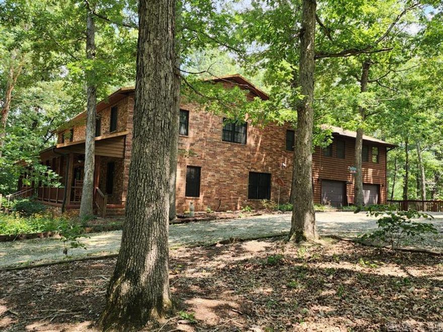 This 4992 sq ft brick home sits on 12.31 tree-covered acres with a creek, shop  and metal barn. The exterior features stained cedar, a wrap-around deck, a metal roof, and a large front porch. Inside, the main level has an extra-large living room, spacious dining room, and a kitchen filled with cabinets and a breakfast area. The kitchen is designed for cooking, while the dining room showcases the meal.  The home spans two levels, each self-sufficient. The second level has a family room with built-in shelving, three bedrooms with walk-in closets, and a hall bathroom. The primary bedroom on the lower level has a huge walk-in closet, abundant natural light, and a bathroom with double sinks, a separate vanity, and a shower. Attached guest quarters include one bedroom, one bathroom, a kitchen, living room, snack bar, dining area, private entrance, and access from the main home's upper level. The wrap-around deck and front porch provide outdoor relaxation spaces. The property has 5 bedrooms, 3.5 bathrooms, a game/family room, a workshop garage, and a metal barn with its own gated entrance. This property offers natural beauty and expansive living spaces for comfortable and private living.