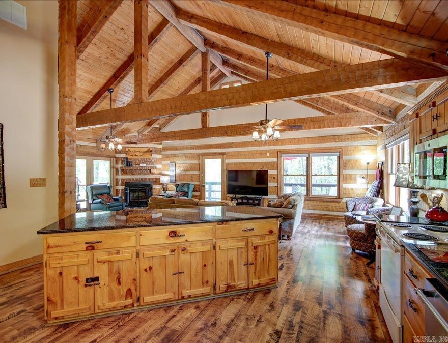 Discover your peaceful forest retreat in this inviting 3-bedroom, 3-bathroom one of a kind hewn log cabin nestled on a quiet cul-de-sac in Hot Springs Village. With high cathedral ceilings on the main floor, this fragrance-free cabin feels like a private mountain escape — and your perfect getaway.  Step inside to a chef’s-ready kitchen featuring sleek black granite countertops, flowing effortlessly into a spacious open living area with a cozy fireplace. The living area opens to a delightful wrap-around deck — your private front-row seat to deer sightings, birdwatching, or quiet family moments.  The main level hosts the luxurious master suite, complete with a king bed and spa tub ensuite, plus a guest suite with its own bathroom and shower. A bright sunroom awaits for meals or game nights with nature as your backdrop.  Downstairs offers additional sleeping space with three more beds and a full bath with shower. Outside, a firepit area with colorful seating invites you to toast marshmallows under the stars.  Located inside the gated Hot Springs Village, you’ll have access to 11 lakes, nine golf courses, a sand beach, marina, restaurants, and trails