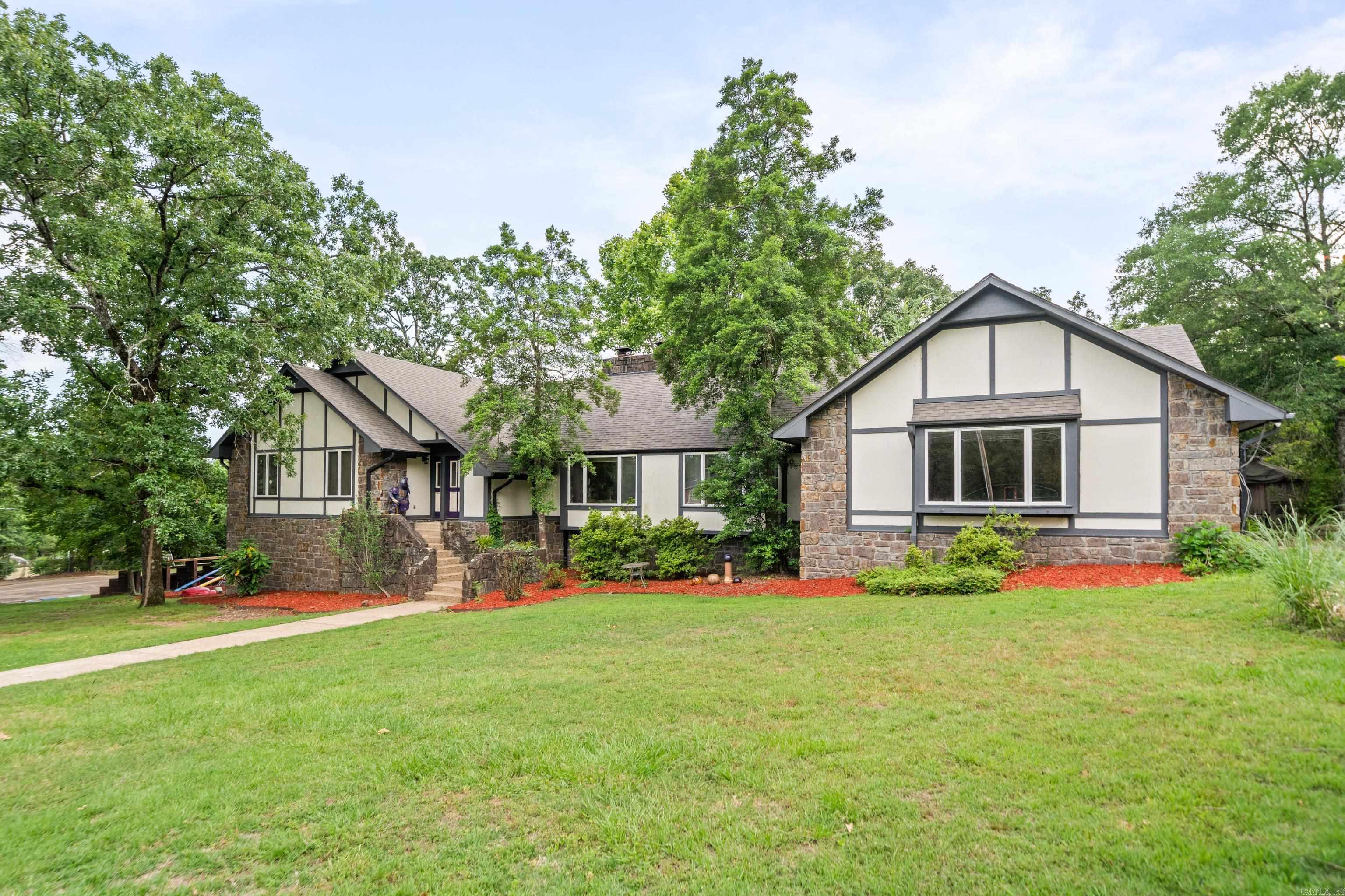 Experience timeless charm and elevated living in this Tudor-style 5-bedroom, 3 full bath, 2 half bath home, nestled on 3.49 wooded acres not far from Lake Hamilton! With over 4,000 sq ft of beautifully designed space, this home is as functional as it is unforgettable. Enjoy a chlorine pool, hot tub and an art-filled outdoor kitchen that creates a vibrant space to cook, gather and entertain. Relax beneath the shaded cabana lounge or shoot hoops on your private basketball court. From the gorgeous rock exterior to the unique design elements, this home blends old world charm with a vibrant, creative energy that's perfect for making lasting memories. Perfect for nightly rentals!