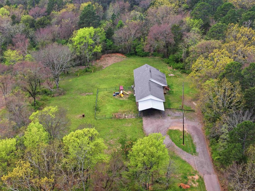 Perched on a scenic hill just minutes from the lake, this charming property offers the perfect blend of privacy, space, and opportunity. Set on 6 wooded acres, the land provides a peaceful natural setting with endless possibilities—whether you envision trails, a garden, or future expansion. Enjoy quiet mornings and relaxing evenings on the inviting front porch, surrounded by the sights and sounds of nature. The fenced-in backyard is ideal for children or pets to play safely, adding to the home’s family-friendly appeal. Inside, you’ll find a flexible layout that includes a bonus room currently being used as a fourth bedroom—perfect for guests, a home office, or a hobby space. The oversized two-car garage offers ample room not only for vehicles but also for extra storage or even a fishing boat, making it a great fit for outdoor enthusiasts. With its serene setting, functional features, and proximity to the lake, this property is a rare opportunity to enjoy country living with convenience close by.
