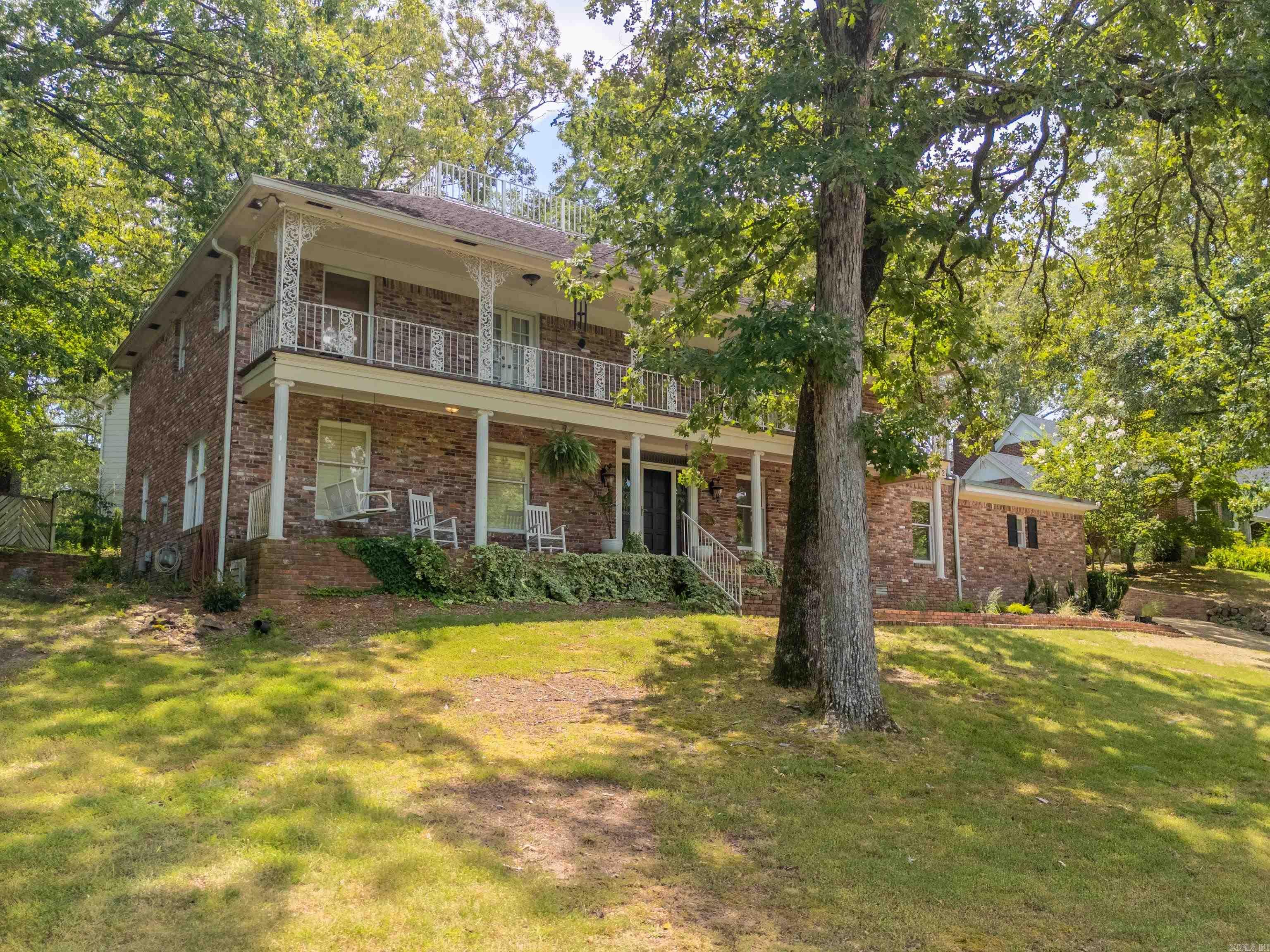 This Southern Colonial estate sits proudly atop a hill in the highly sought-after Eastgate Subdivision. Priced below market value, itās hands-down the best deal in its price range. Encompassed by mature trees on over half an Acre, this property offers rare privacy and space in a prime location. From the moment you arrive, the double front porches and ornate wrought iron detailing flaunt true Southern charm with a touch of New Orleans flairāperfectly suited for a stately Arkansas home. Inside, the living room welcomes you with exposed wood beams and a cozy wood-burning fireplace. The kitchen features abundant cabinet & counter space, with warm terra cotta tile underfoot and picturesque views of the terraced patio and wooded hillsideāa peaceful backdrop while cooking/entertaining. Outside, brick steps lead from the patio to a concrete pad, the perfect area to roast marshmallows around a fire pit with friends. The flexible floor plan includes 4 bedrooms, 3 full baths, a main-level office with beautiful French doors, a spacious den/game room, a laundry room with a built-in desk, and a workshop attached to the garage; And hereās the real bonus: this home holds a city short-term rental.