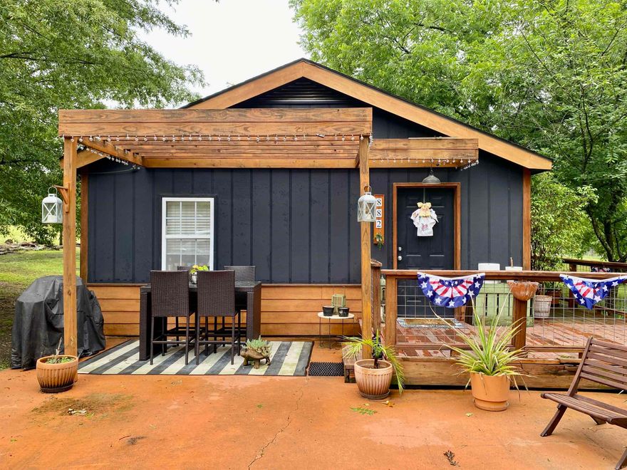 Warm and welcoming best describe this beautiful bungalow, perfectly nestled on a park-like, tree-covered lot on the edge of Clarksville. The open living and dining area offers a comfortable space to gather, while the kitchen features a breakfast bar, ample cabinetry, and a bonus prep sink—ideal for home cooks. The spacious laundry room includes a stand-up shower and has enough room to easily convert into a full second bath.  Enjoy over 600 sq.ft. of outdoor living space with double decks and a patio—perfect for relaxing or entertaining. The level lot is graced with established pecan trees and offers plenty of space to add a garden. This charming oasis is a must-see!  A new roof will also be installed prior to closing.  The larger outbuilding sits just off the property line and will convey if the buyer wishes to move it. Dog panels do not convey.