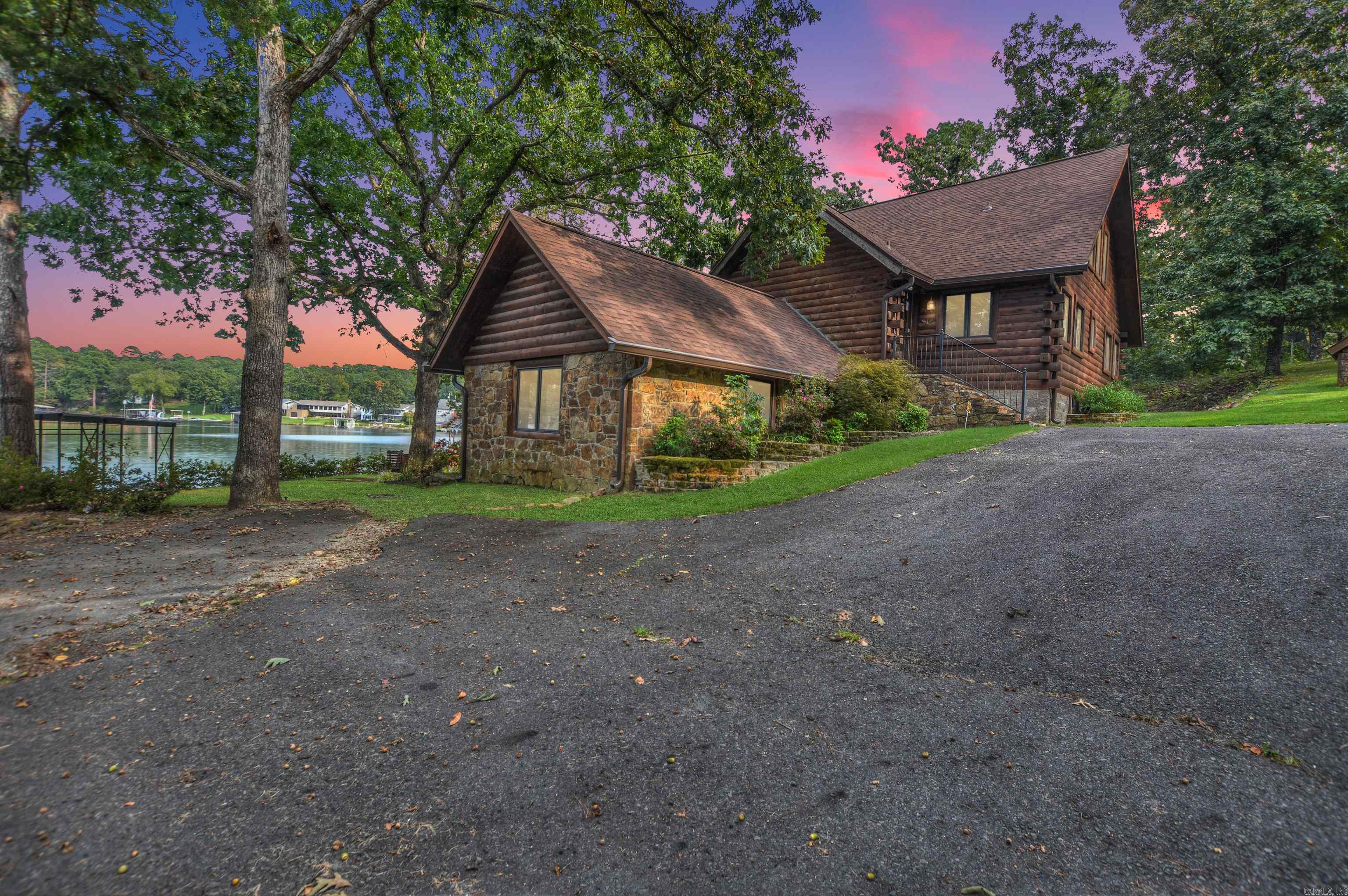 Lake Hamilton waterfront retreat! This 3,264 sq. ft., 3-story log cabin offers 149’ of shoreline with stone seawall, private boat ramp, covered double boat dock, and separate swim dock. Built in 2002 on a .5-acre treed lot with circle drive and detached workshop, it’s ideal as a primary residence, getaway, or nightly rental (no restrictions). The walk-out lower level features a game room, family room, kitchenette, bedroom, bath & laundry. Main level has 2 bedrooms, bath, open kitchen, family room with cozy stove, and walls of glass opening to an expansive deck. Upper level offers a private suite with bedroom, bath, and dual walk-in closets. Hardwood & tile floors plus walls of glass throughout. Proven rental history—move-in ready for lake living or investment!
