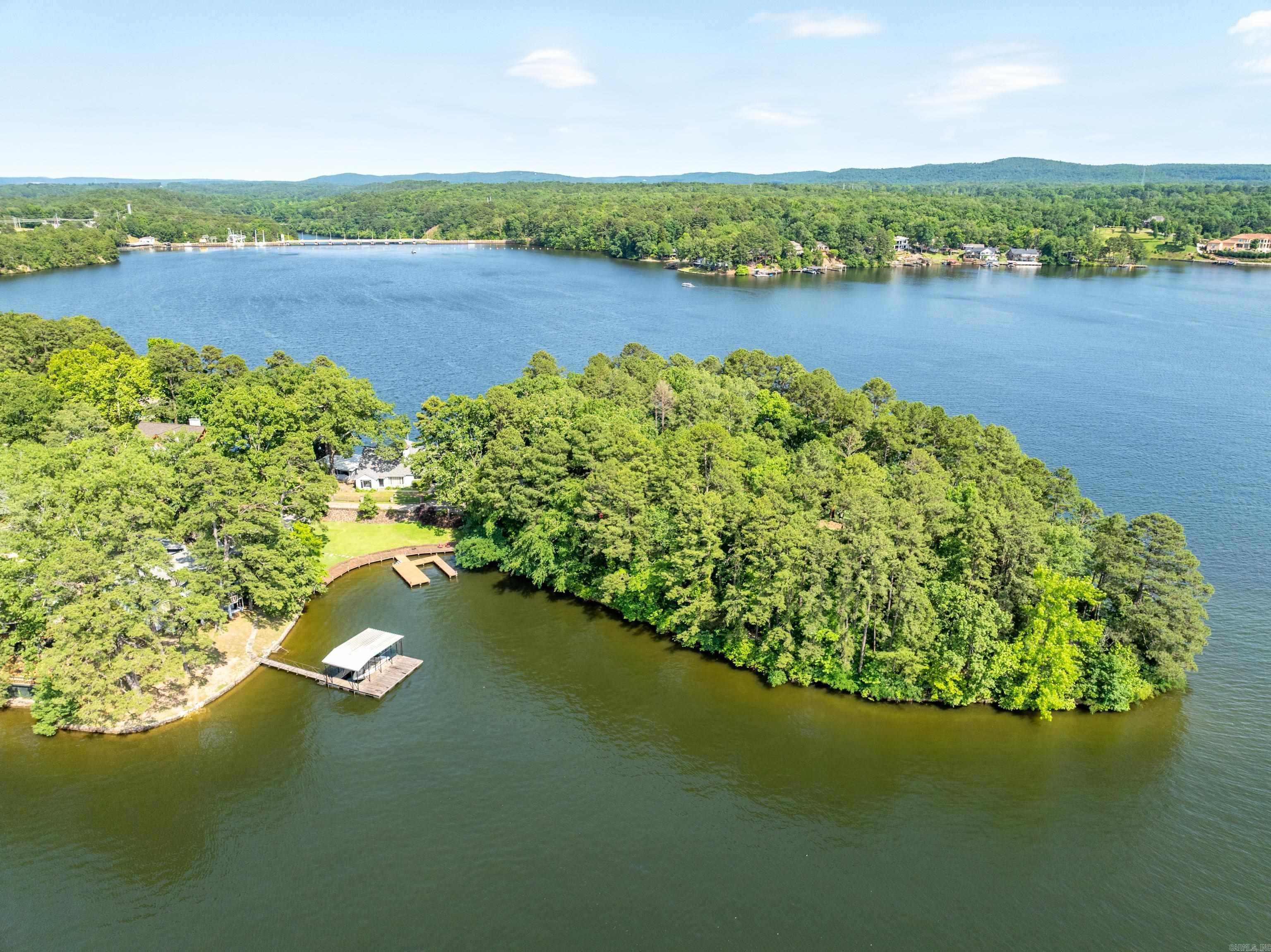 Come see this once-in-a-lifetime property perched on the shores of Lake Hamilton in Hot Springs, Arkansas! Situated on a majestic 2.12-acre point, this extraordinary estate offers unparalleled breathtaking views of sunrises and sunsets on Lake Hamilton's serene waters. Whether sipping your morning coffee or hosting guests for dinner, you will be captivated by the natural beauty that is right outside your door. With plenty of area for outdoor living, you can enjoy direct access to the lake with over 1081 feet of waterfront. Recreation and entertainment spaces are abundant with outside decks hovering right over Lake Hamilton. Dive into the serene waters from your own “high dive” board, moor your watercraft, or soak up the sun and take in the spectacular views that stretch for miles. The waterfront boathouse with two private slips is perfect for facilitating easy access to all sorts of water activities, including skiing, fishing, or leisurely cruises to soak up the sun. Spacious interiors abound in the 5-bedroom, 3-bath home, which spans 4992 square feet. Luxury details are evident throughout with vintage finishes and tasteful furnishings that enhance its ambiance. ---->